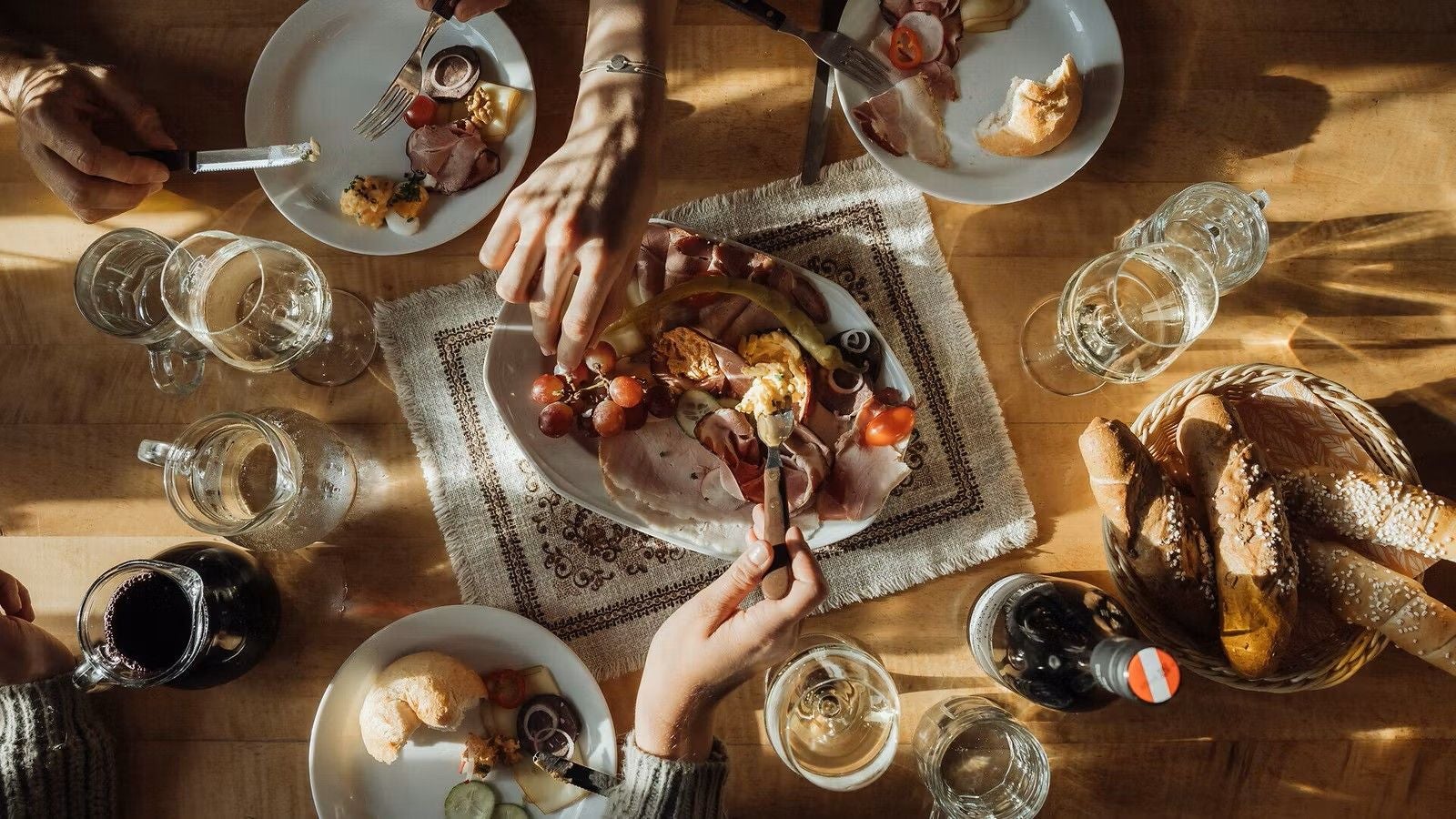Heurigentisch mit Brot, Wurst, Käse, Trauben, Gläsern und mehreren Händen beim Essen.