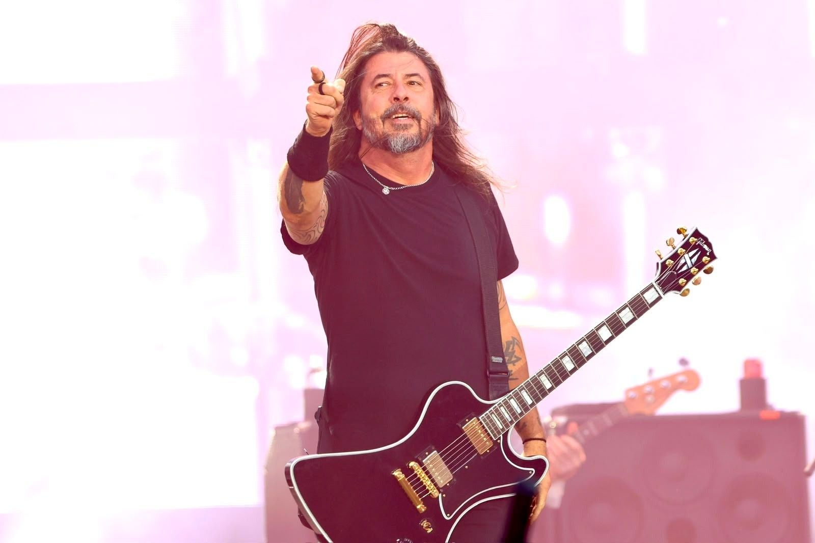 Mann mit Gitarre auf der Bühne, trägt schwarzes Shirt und zeigt nach vorne.