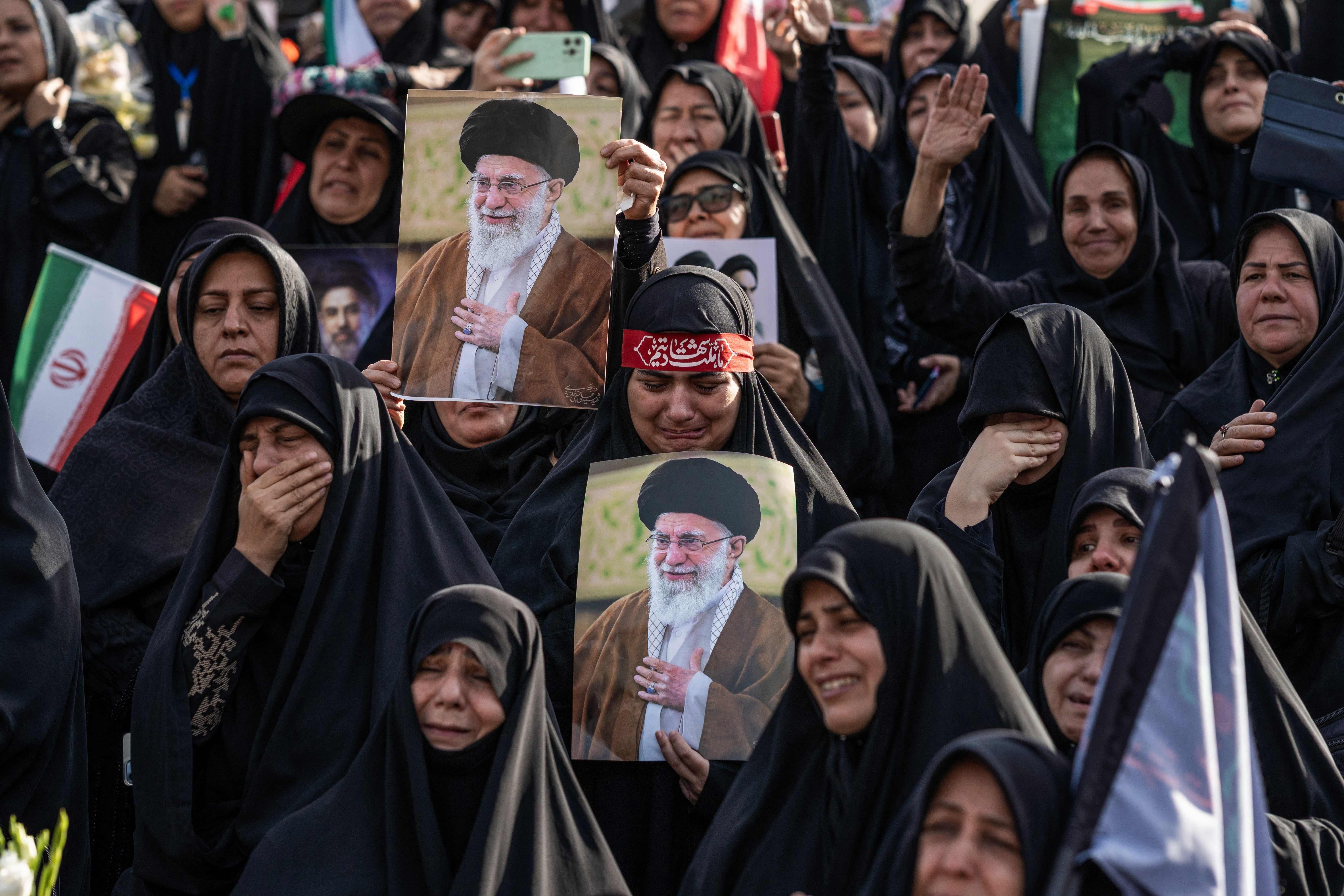 Trauernde Frauen in schwarzen Schleiern halten Porträts von Ayatollah Ali Khamenei und weinen.