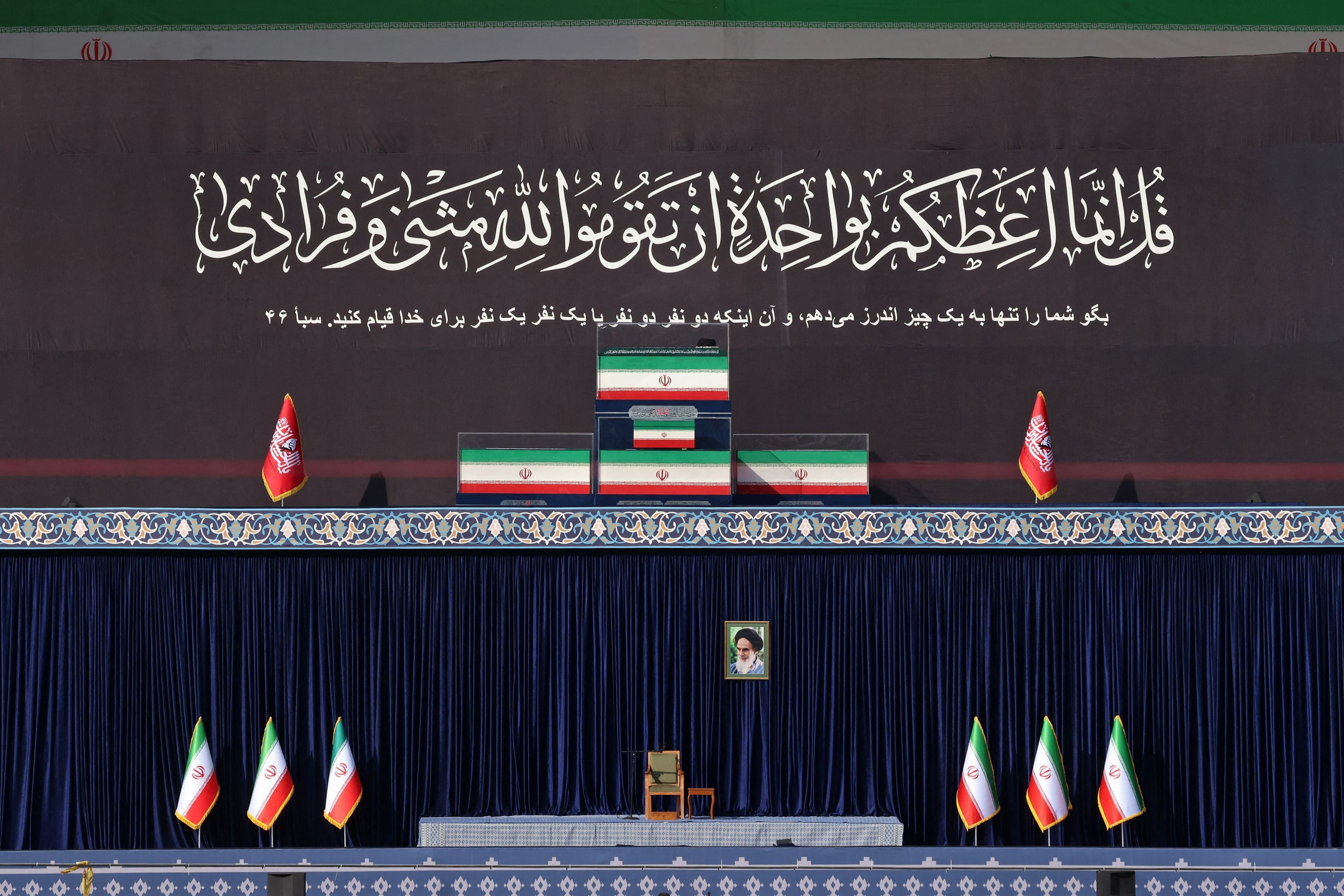 Vier Särge mit iranischen Flaggen stehen auf einer Bühne mit religiösen Bannern und Porträt.