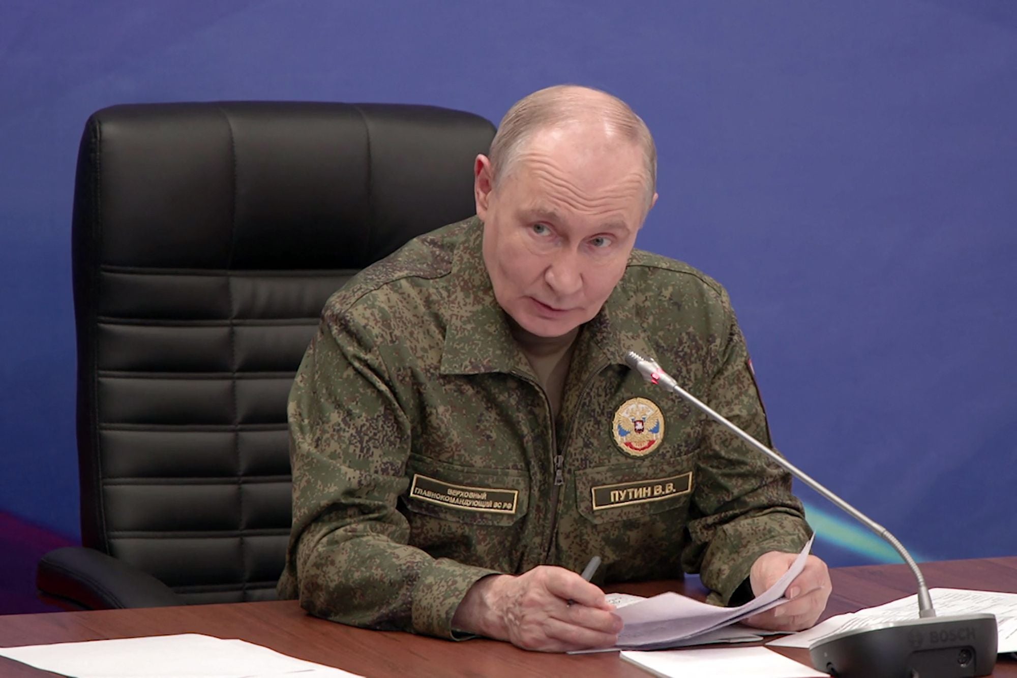 Ein Mann in Militäruniform sitzt an einem Tisch, hält Papiere und spricht in ein Mikrofon.