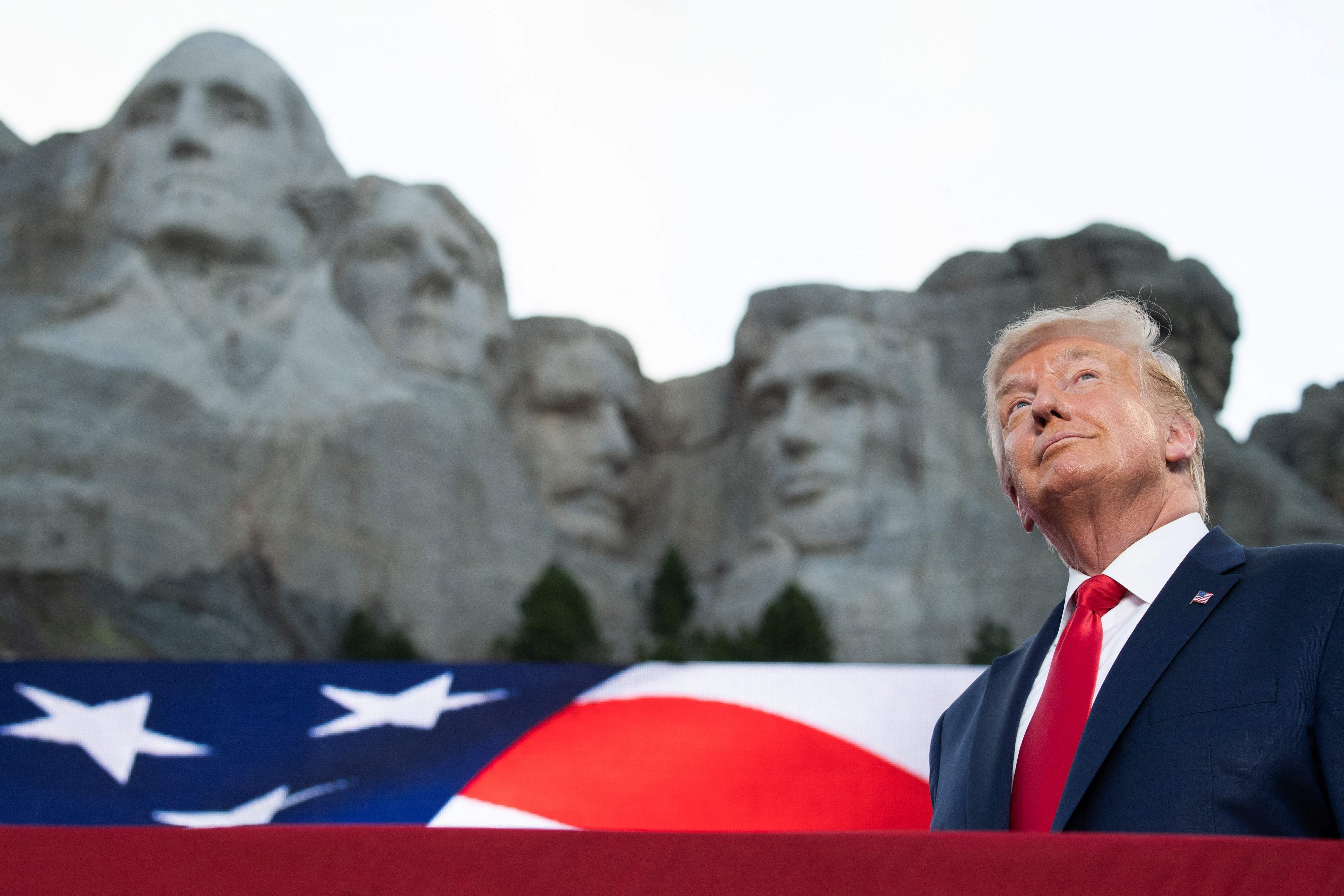 Ein Mann im Anzug steht vor der US-Flagge und Mount Rushmore in South Dakota.