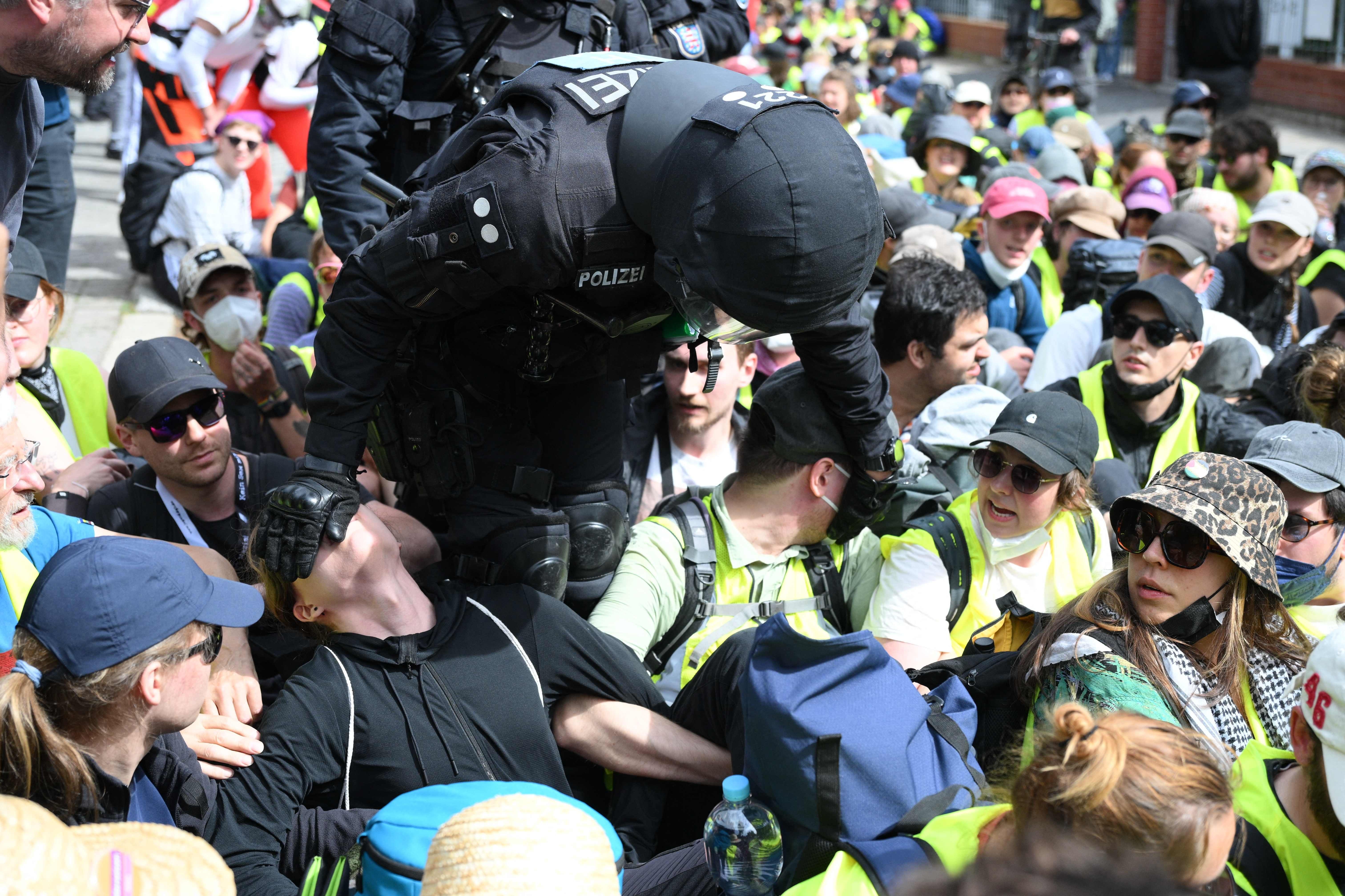 Ein Polizist greift in eine sitzende Gruppe von Demonstranten auf einer Straße ein.