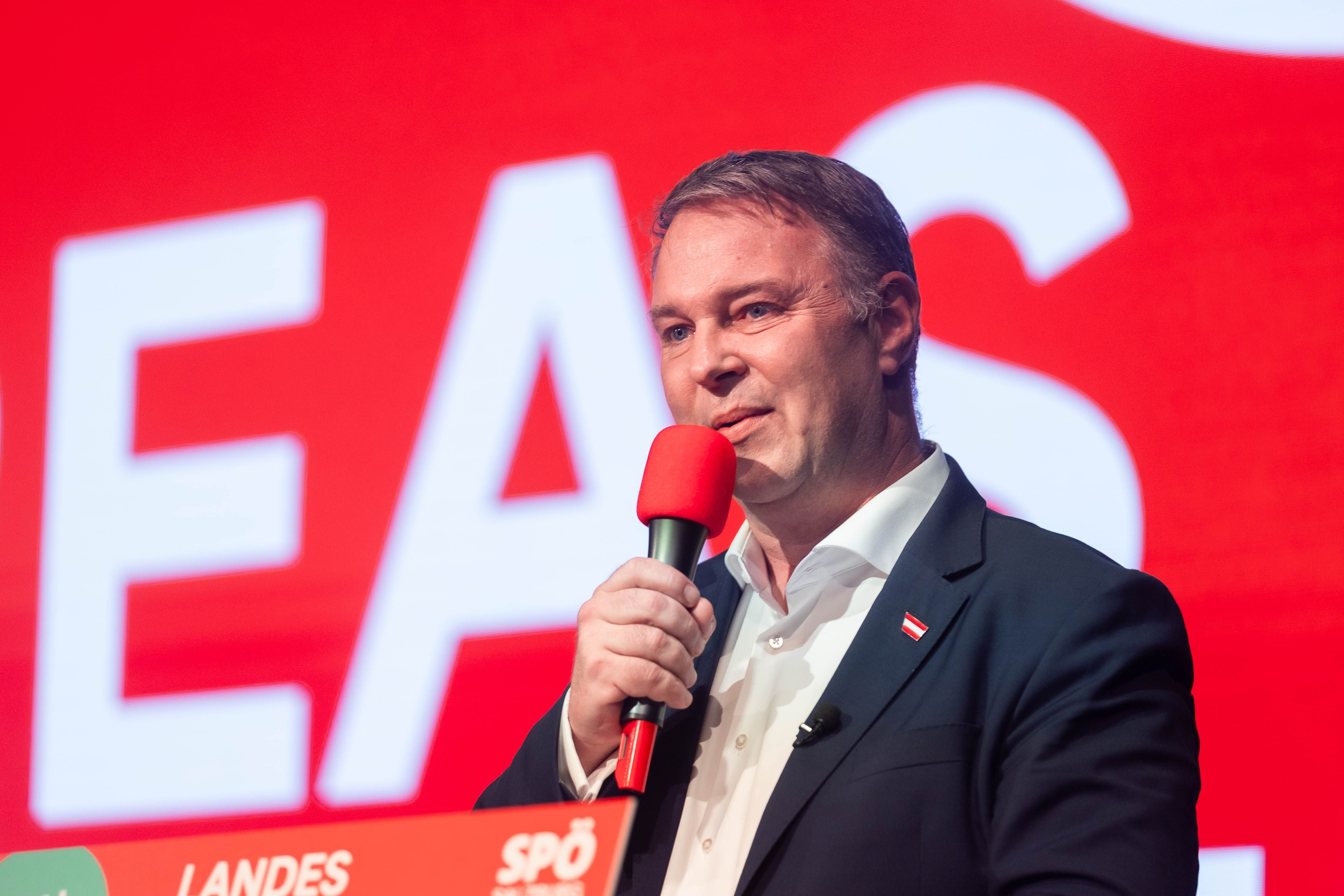 Mann im Anzug spricht mit rotem Mikrofon auf einer SPÖ-Veranstaltung vor rotem Hintergrund.