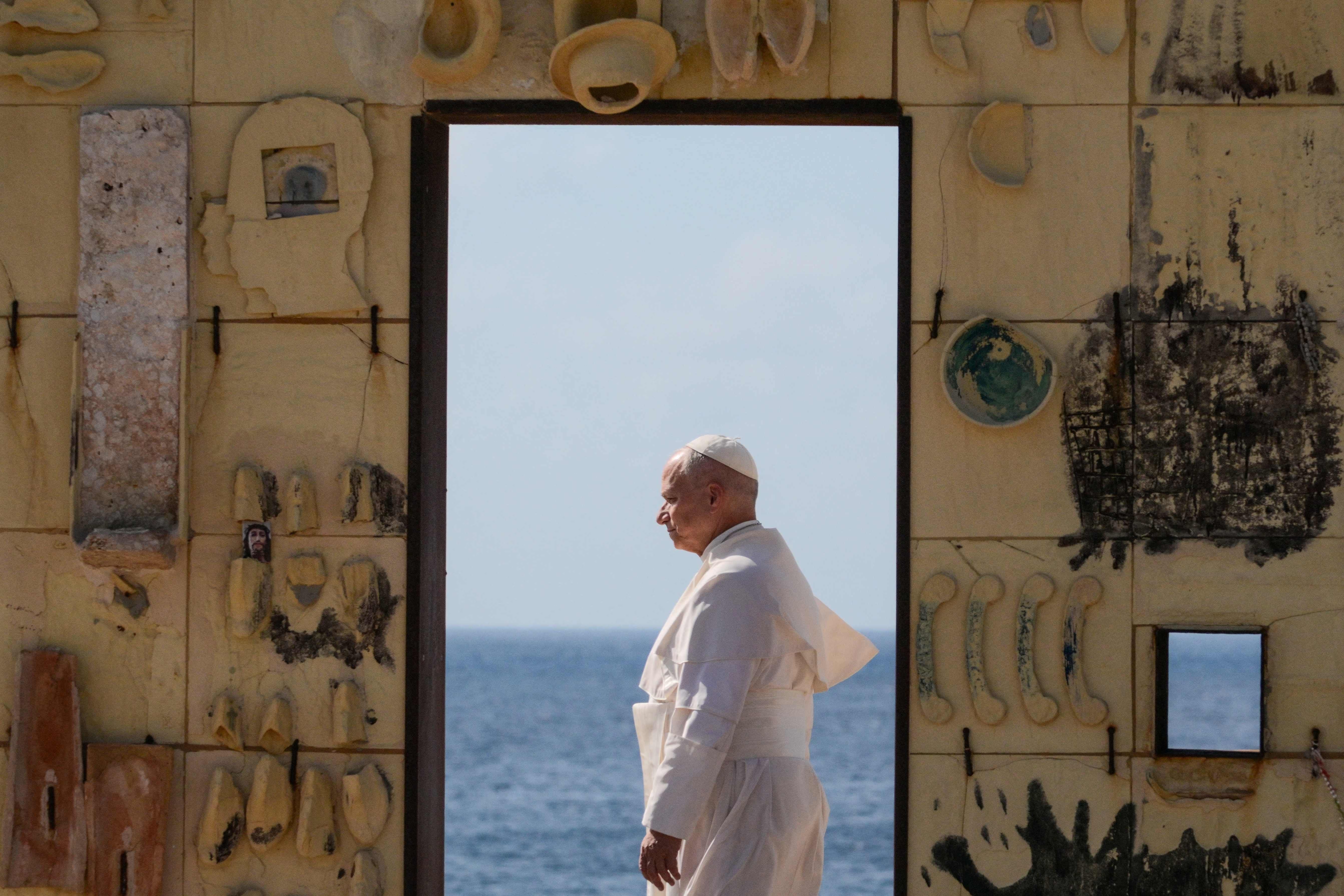 Papst in weißer Kleidung schreitet durch das Tor der Europa-Skulptur mit Meer im Hintergrund.