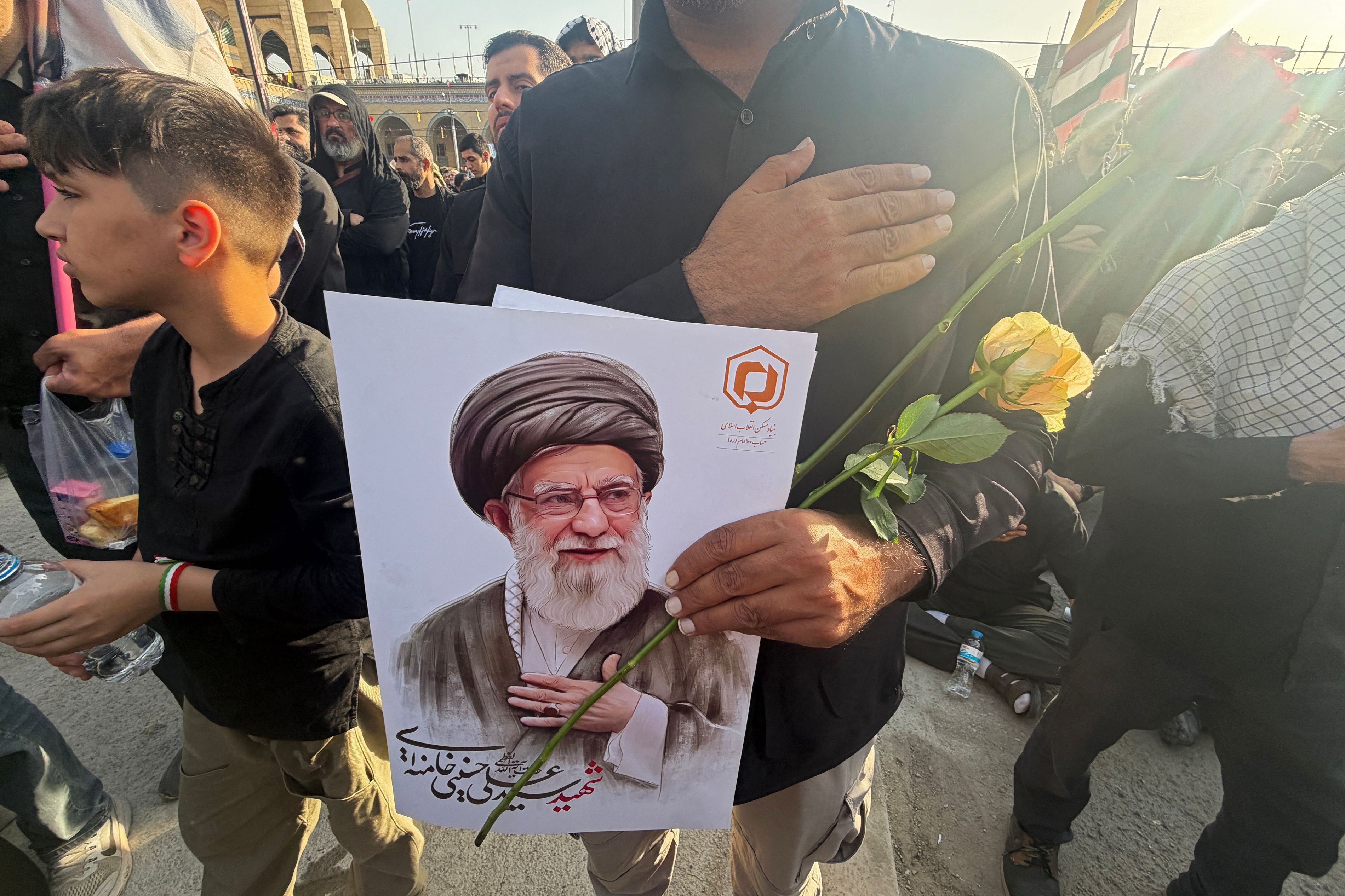 Ein Mann hält ein Porträt von Ayatollah Ali Khamenei und eine gelbe Rose bei einer Trauerzeremonie.