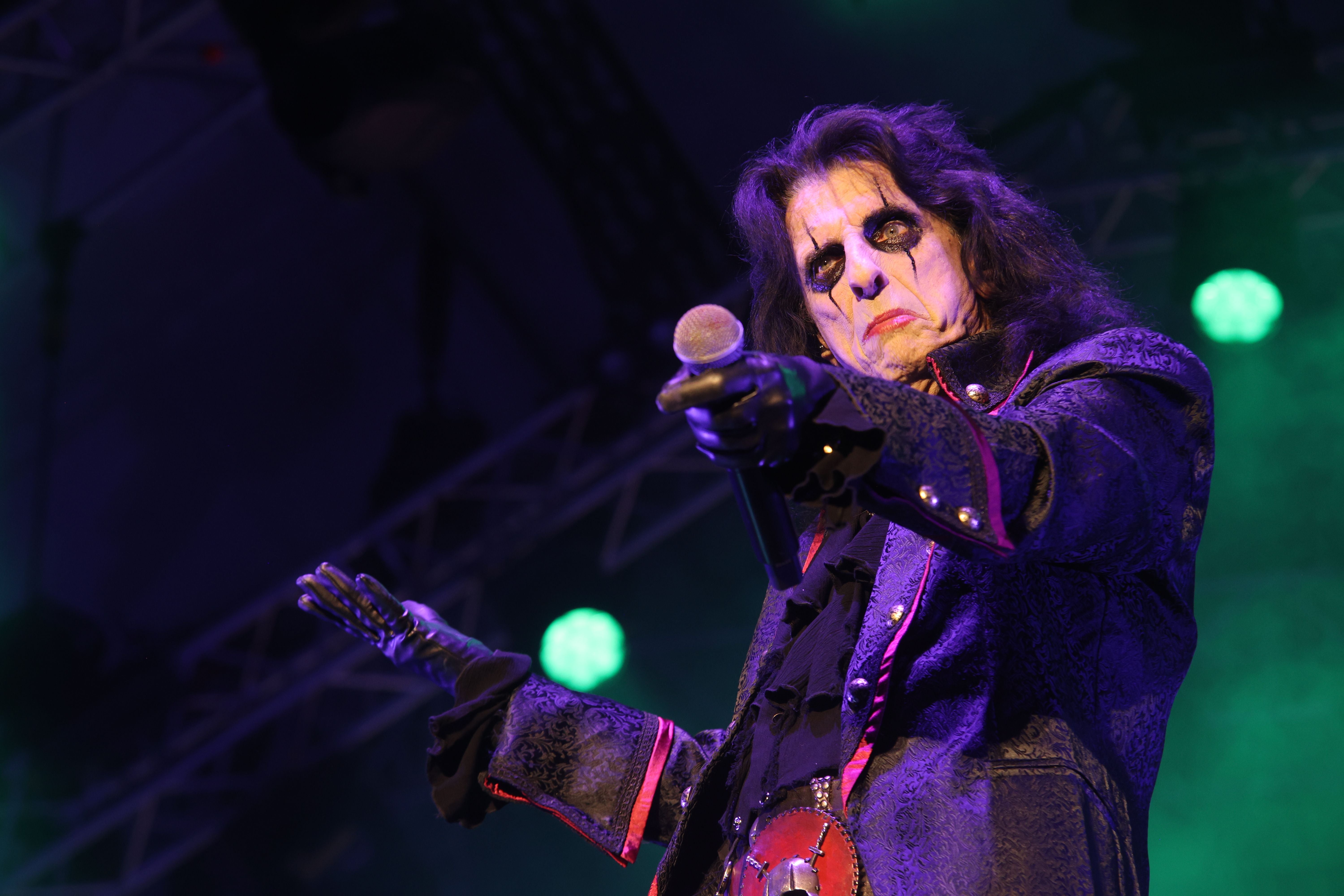 Ein Musiker mit gruseligem Make-up hält ein Mikrofon auf der Bühne unter buntem Licht.