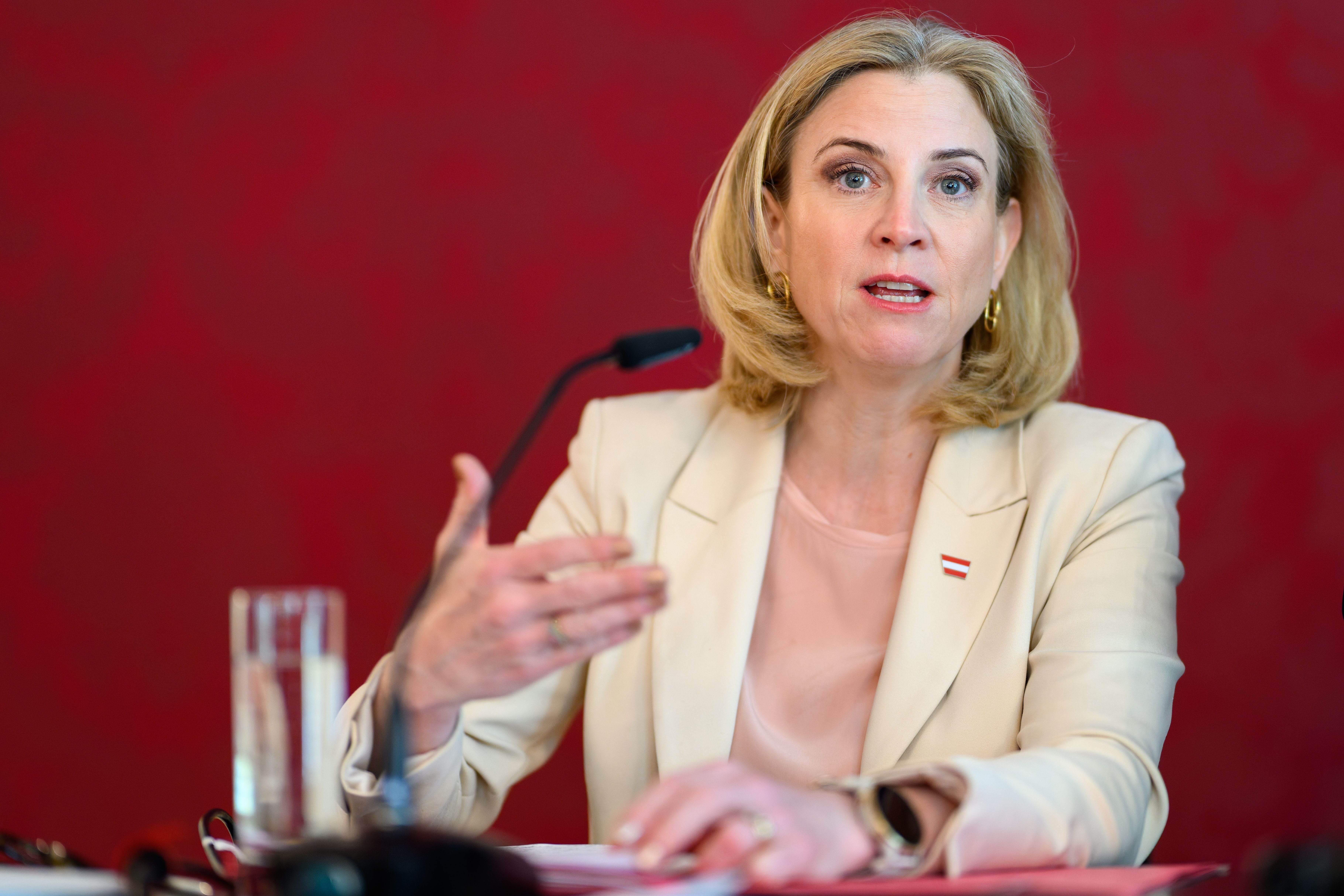 Eine Frau spricht bei einer Konferenz vor rotem Hintergrund und Mikrofon.