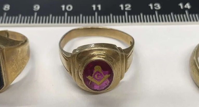 Goldener Siegelring mit Freimaurersymbol und rotem Stein vor einem Lineal.