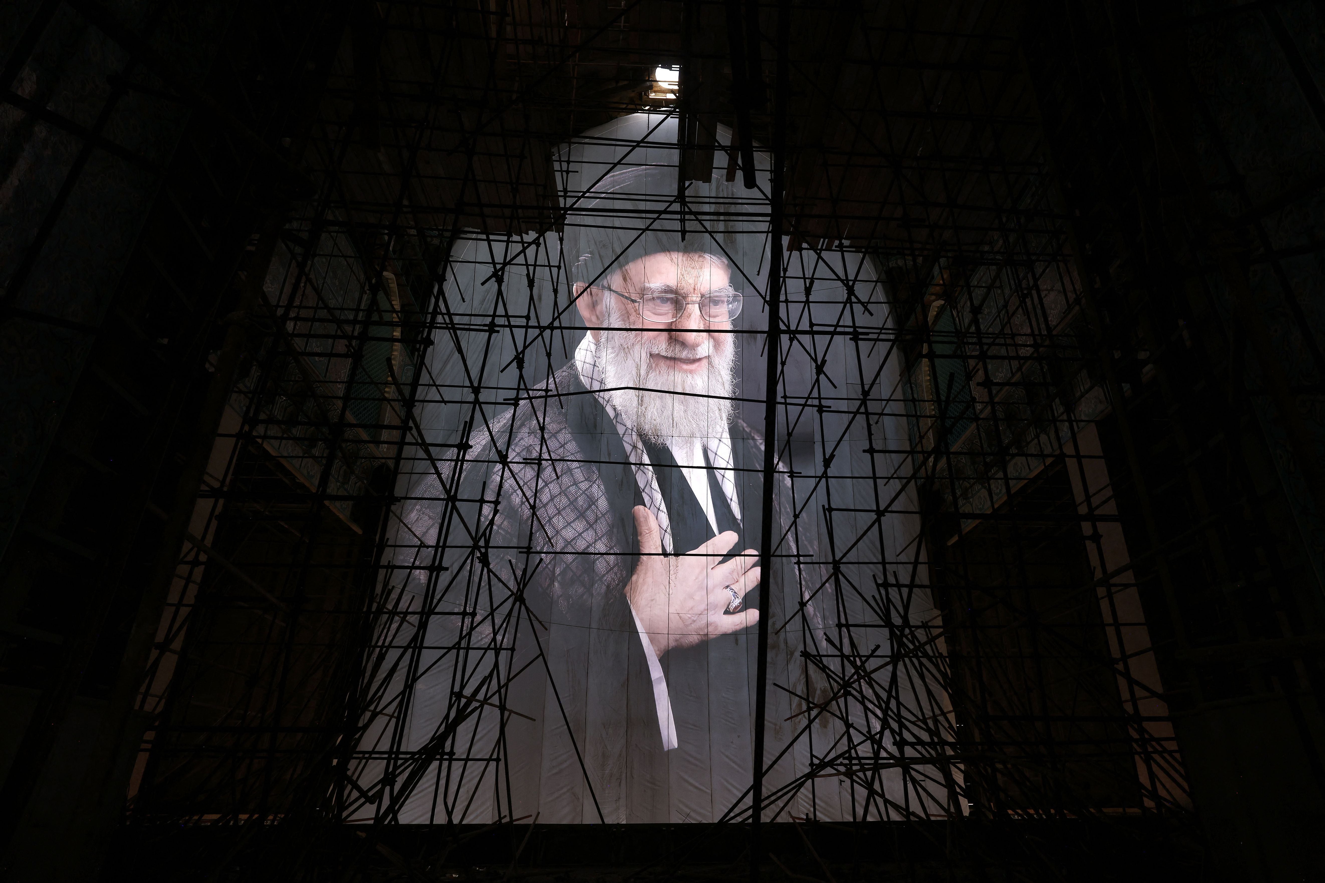 Großes Porträt eines älteren Mannes mit Bart hinter Baugerüsten in einer Halle.