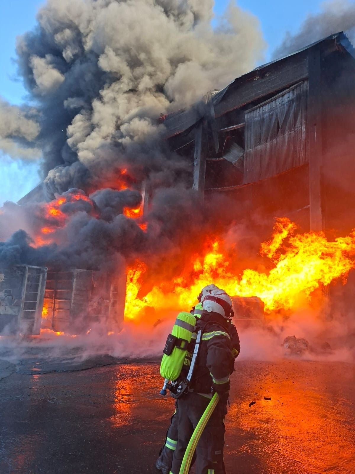 Feuerwehrleute bekämpfen einen Großbrand mit starker Rauchentwicklung an einem brennenden Gebäude.
