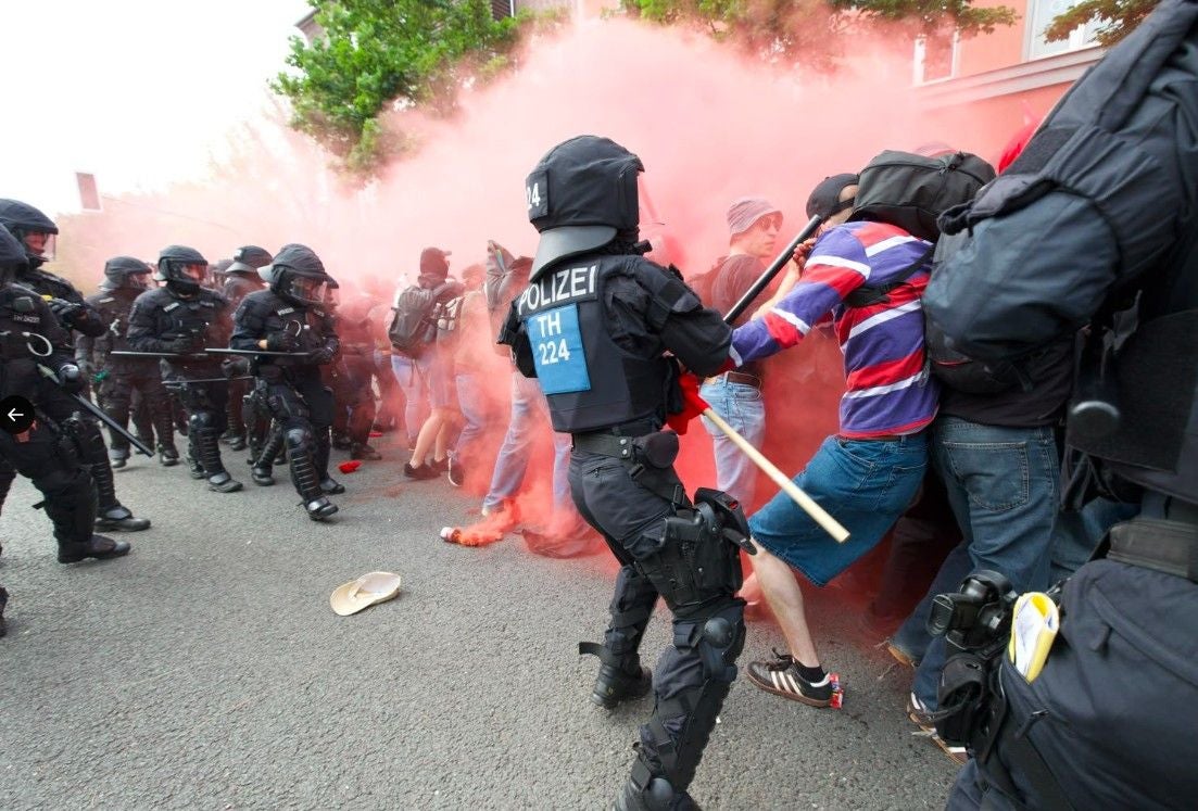 Polizisten in Kampfmontur stoßen auf eine Menschenmenge mit rotem Rauch bei einer AfD-Demo.