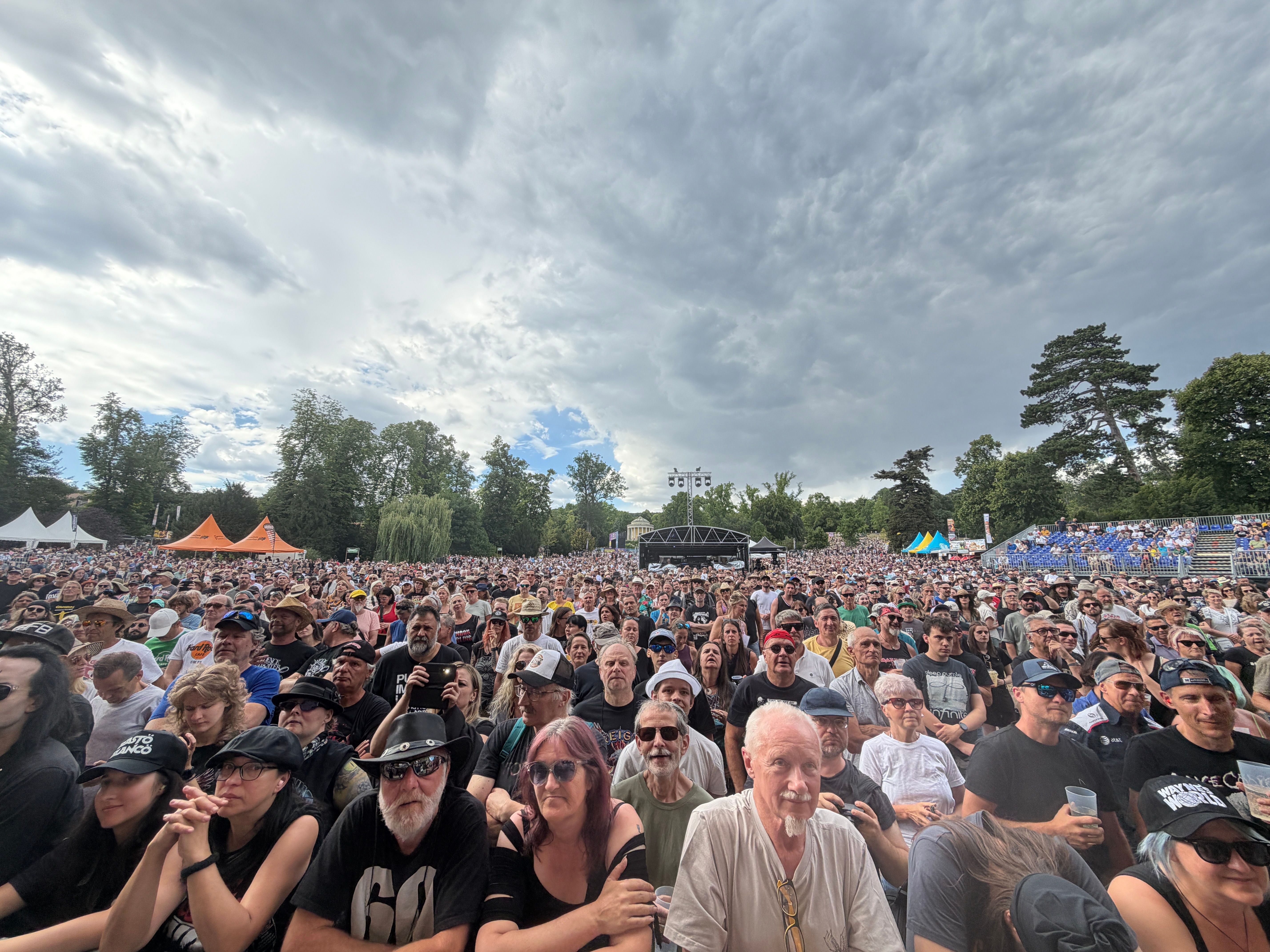 Große Menschenmenge bei einem Open-Air-Konzert im Schlosspark mit bewölktem Himmel.