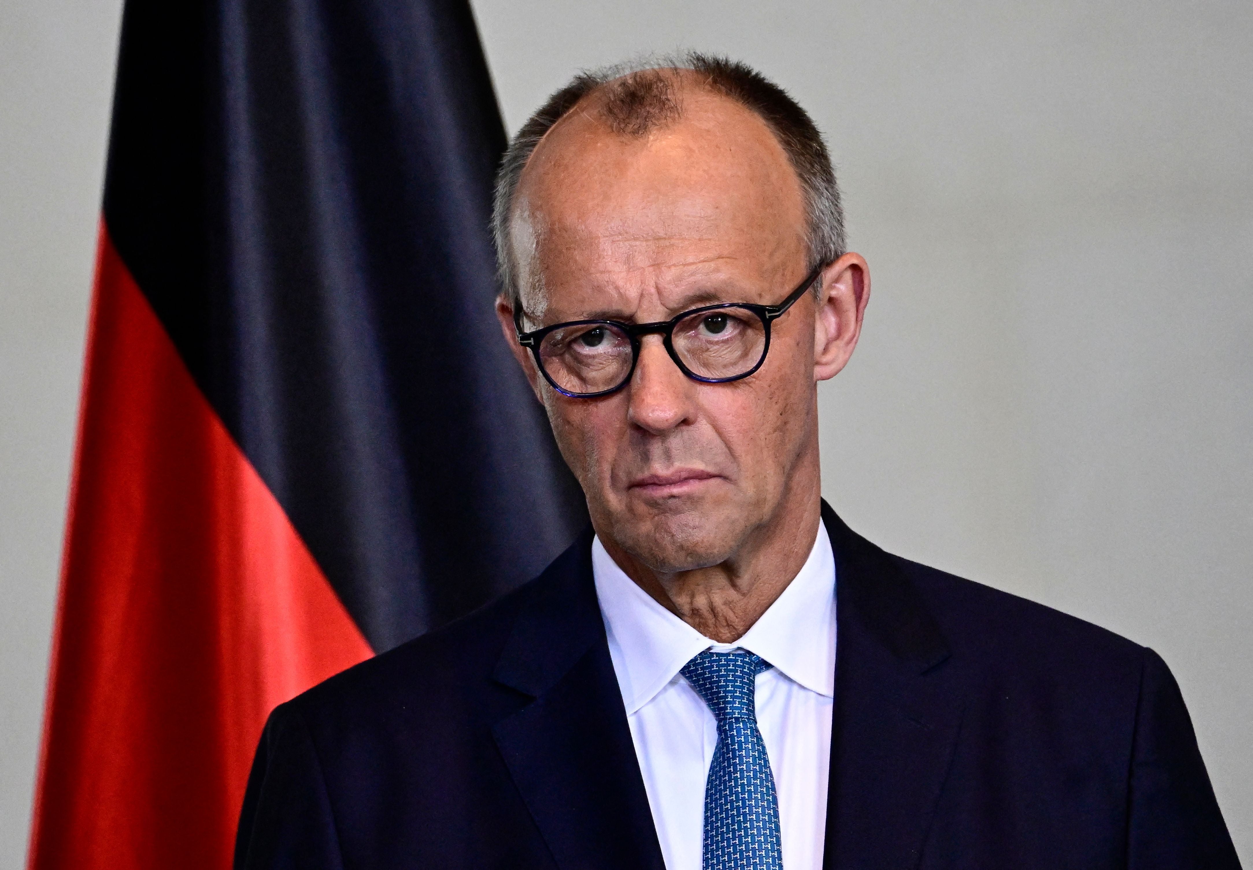 Ein Mann mit Brille im Anzug steht vor einer deutschen Flagge.