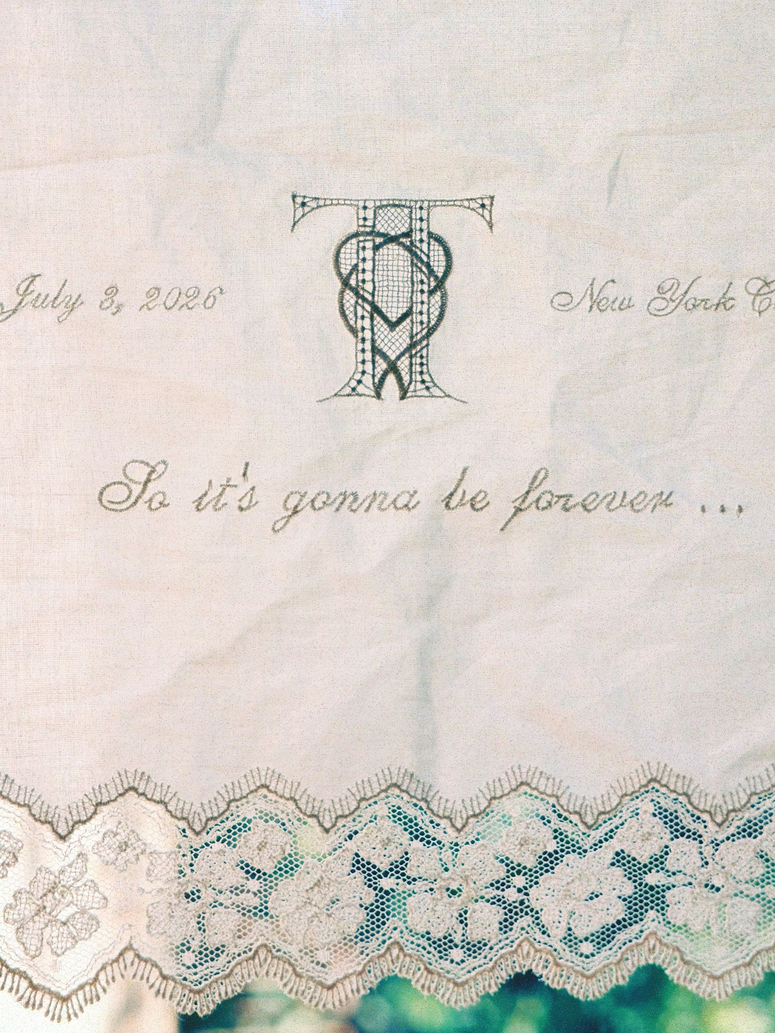 Besticktes Tuch mit Spitze, dem Datum 3. Juli 2026 und dem Satz „So it’s gonna be forever …“.