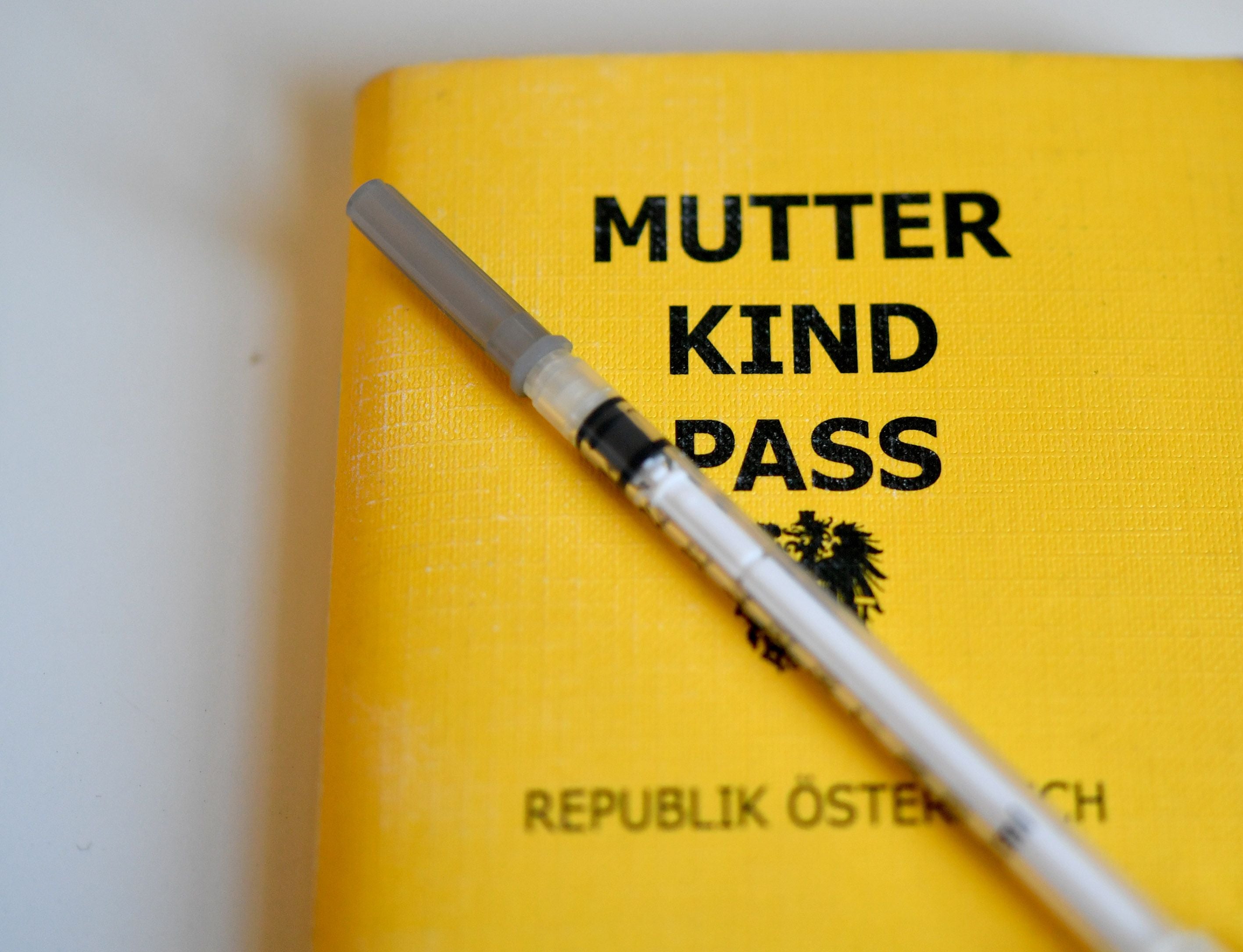 Gelber Mutter-Kind-Pass aus Österreich mit einer Spritze darauf liegend.