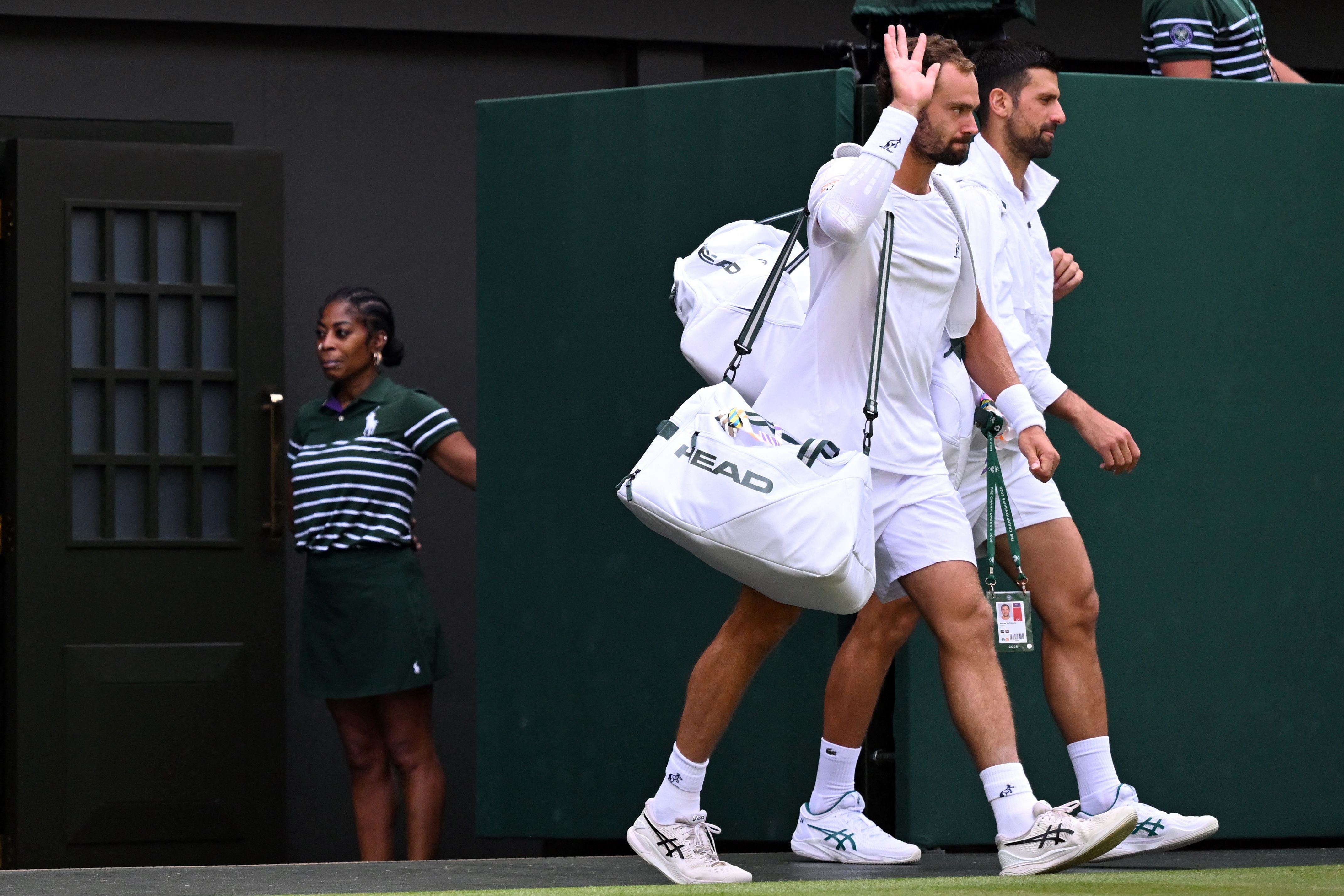 Zwei Tennisspieler betreten das Spielfeld in Wimbledon, einer hebt die Hand zum Gruß.
