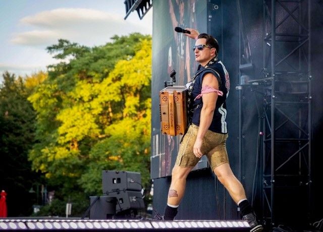 Ein Musiker in Tracht mit Akkordeon steht auf einer Bühne im Freien und hält ein Mikrofon.