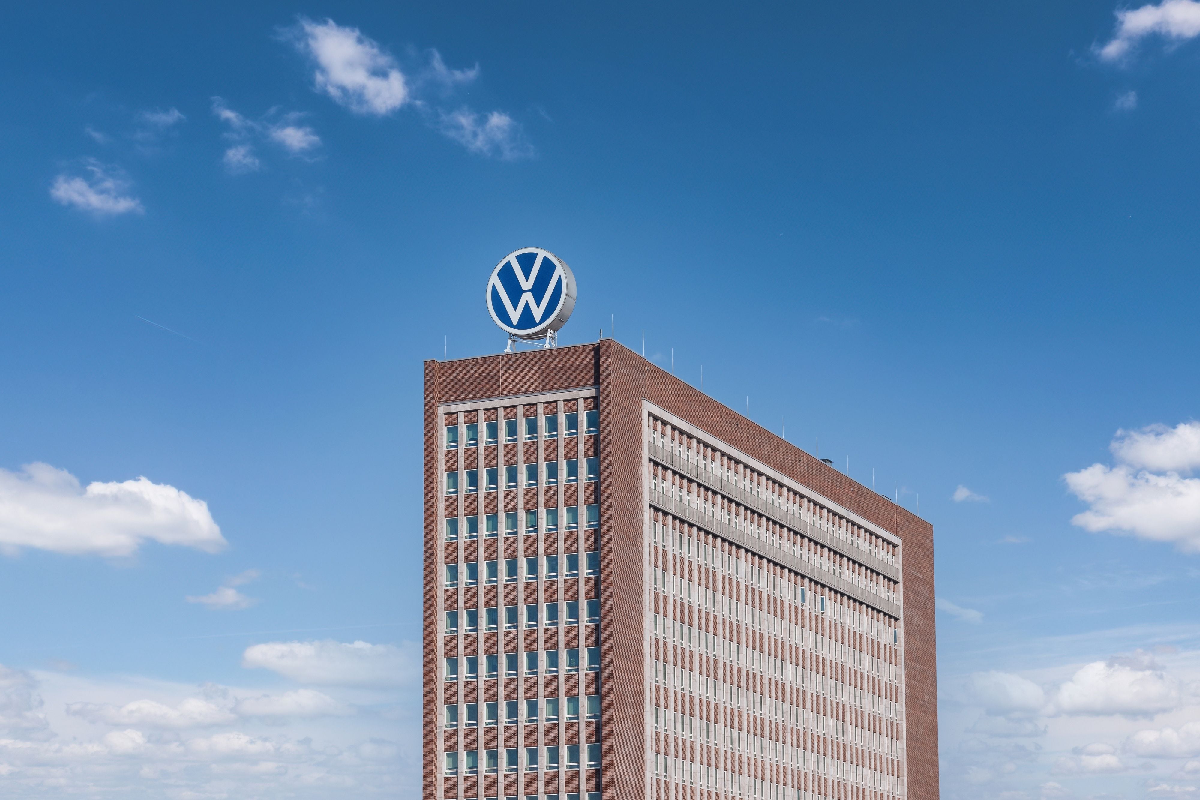 Backsteingebäude mit VW-Logo auf dem Dach vor blauem Himmel in Wolfsburg.