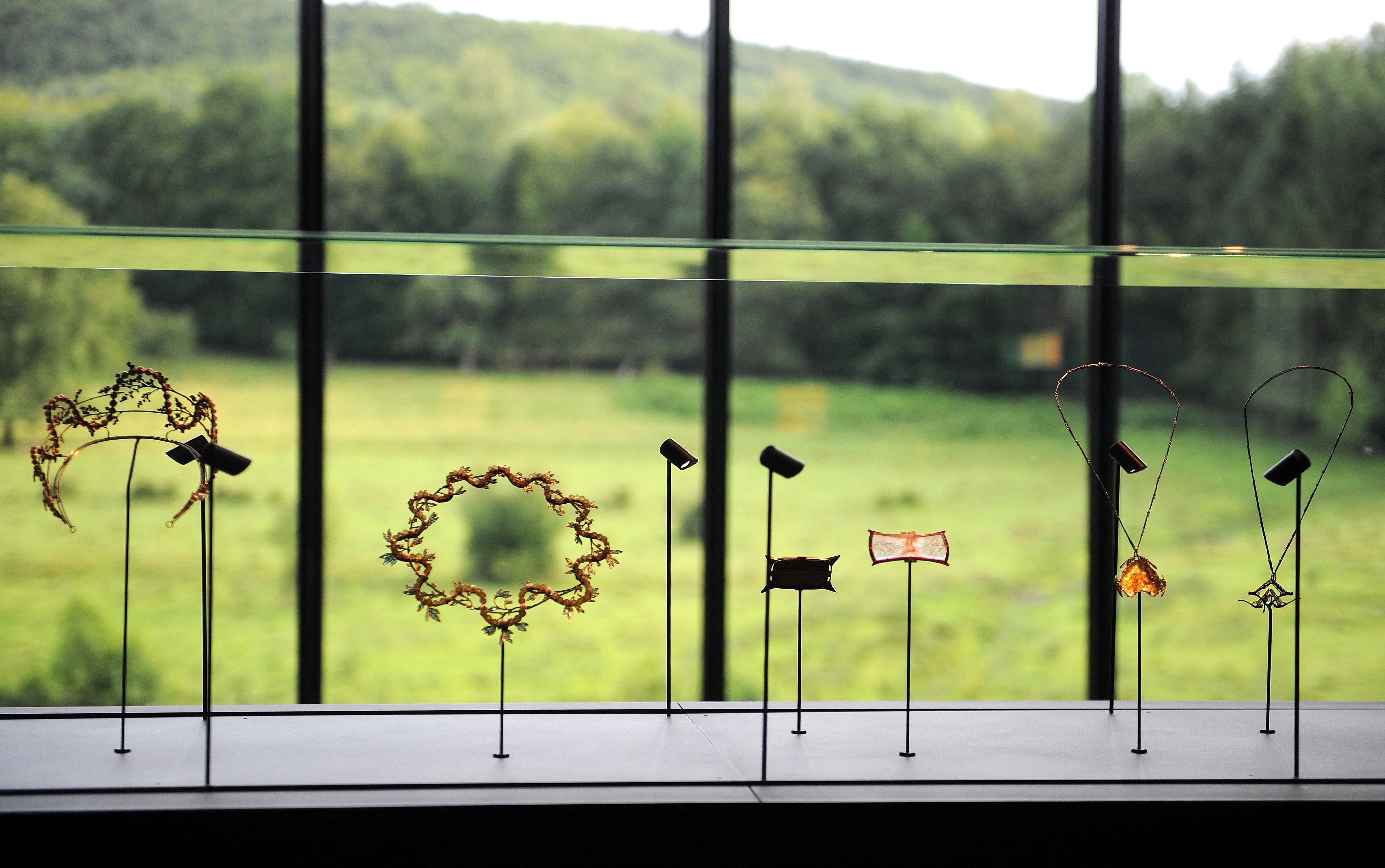 Schmuckstücke von Rene Lalique hinter Glasvitrine mit grüner Landschaft im Hintergrund.