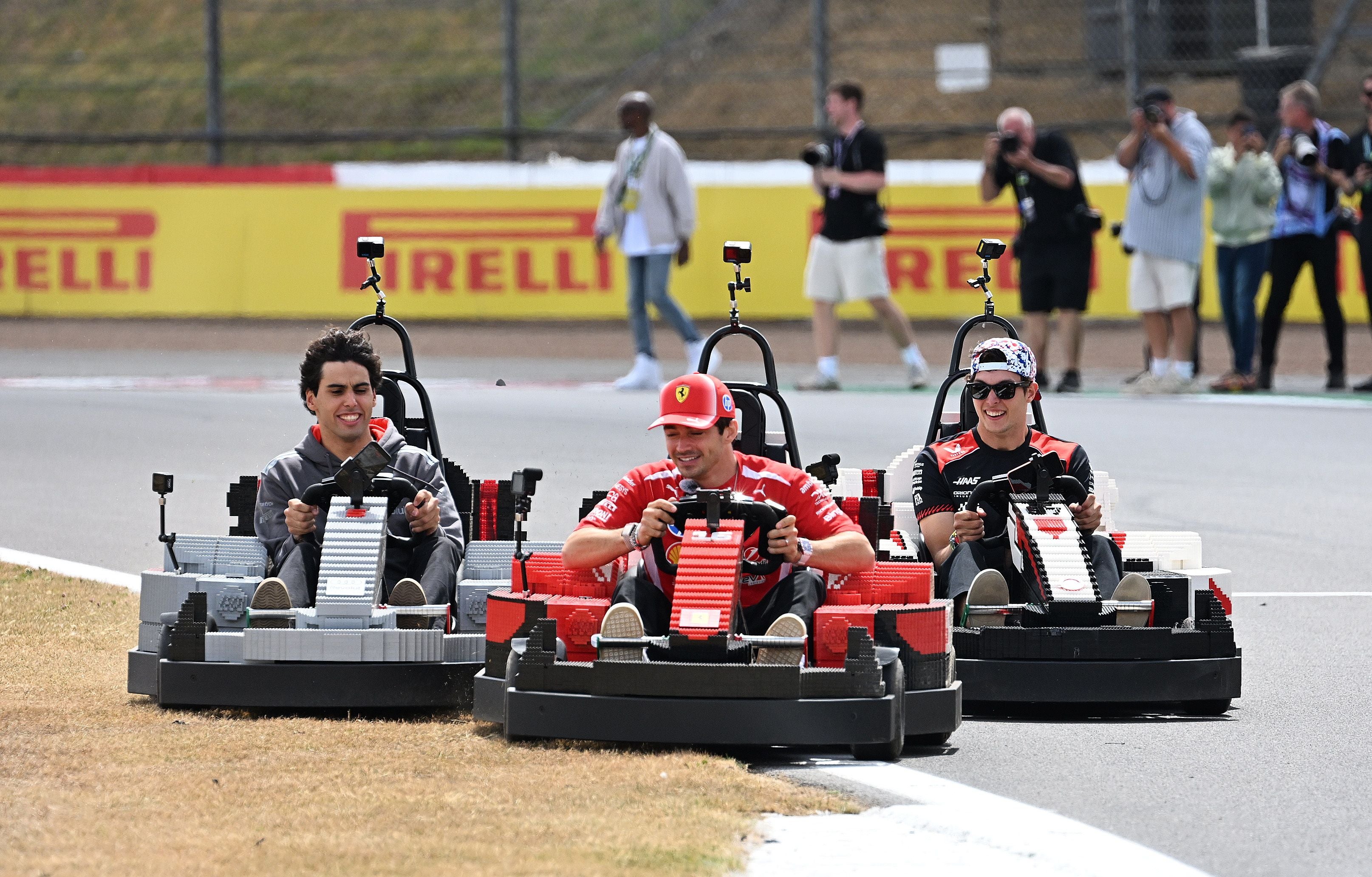 Drei Männer fahren in LEGO-Karts auf einer Rennstrecke, Zuschauer im Hintergrund.