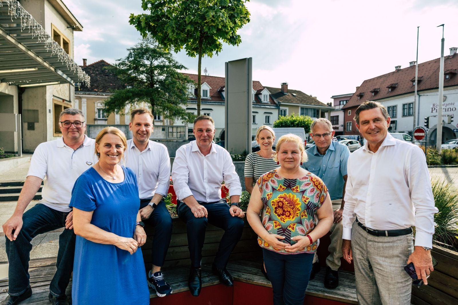 Acht Erwachsene posieren gemeinsam draußen in Traiskirchen für ein Gruppenfoto.