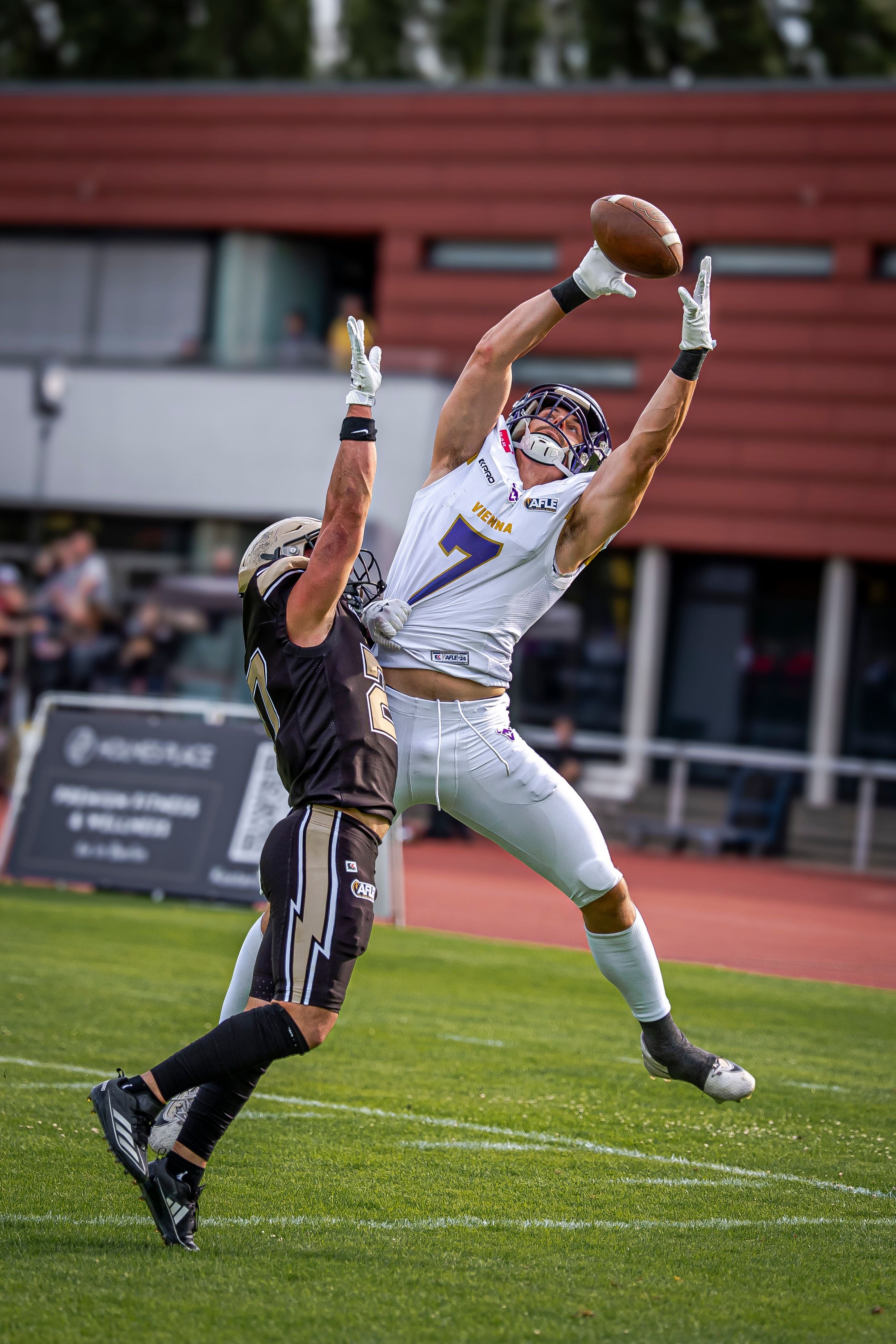 Zwei Footballspieler springen, einer versucht den Ball vor dem anderen zu fangen.