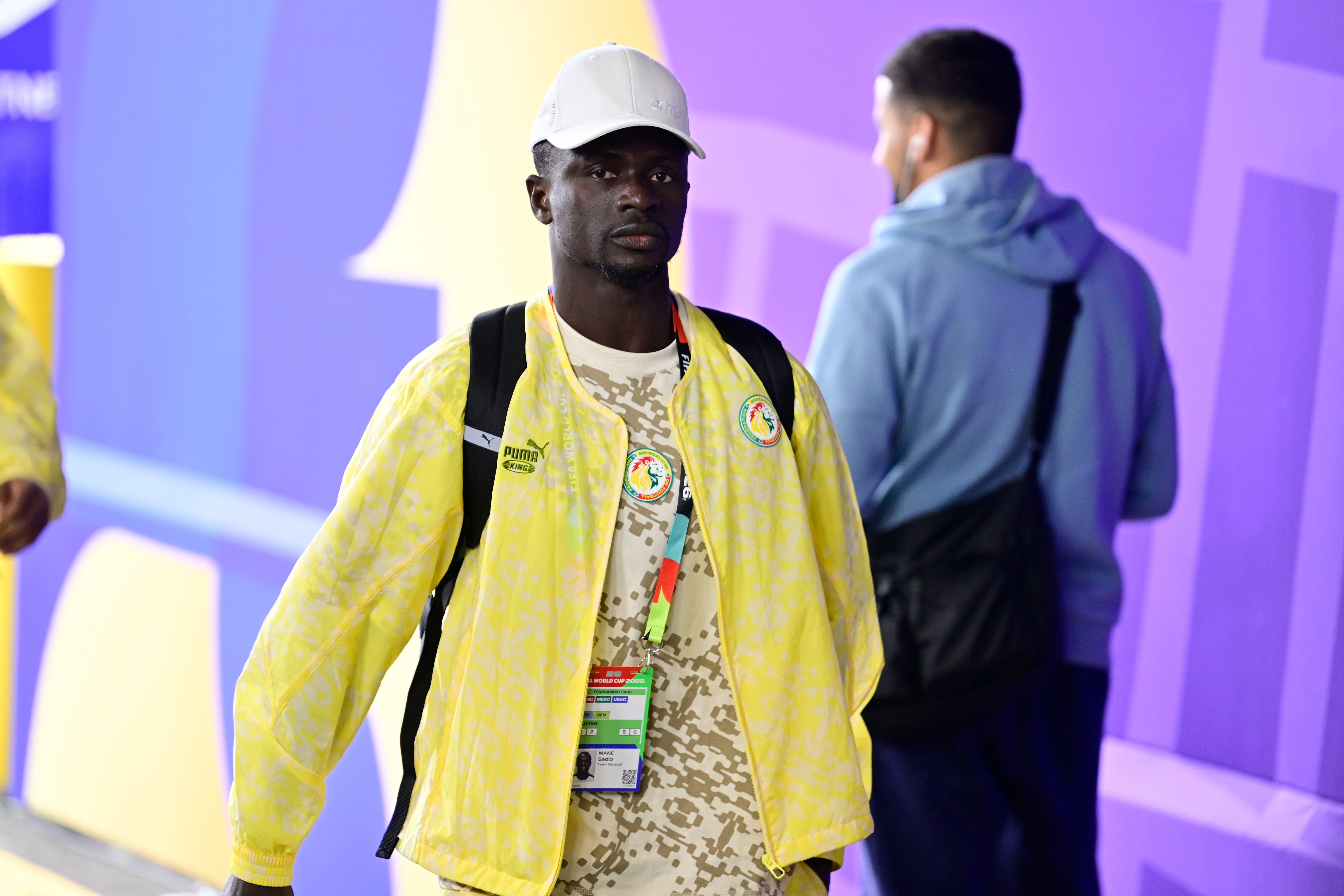 Ein senegalesischer Fußballspieler mit gelber Jacke und weißer Kappe betritt das Stadion.