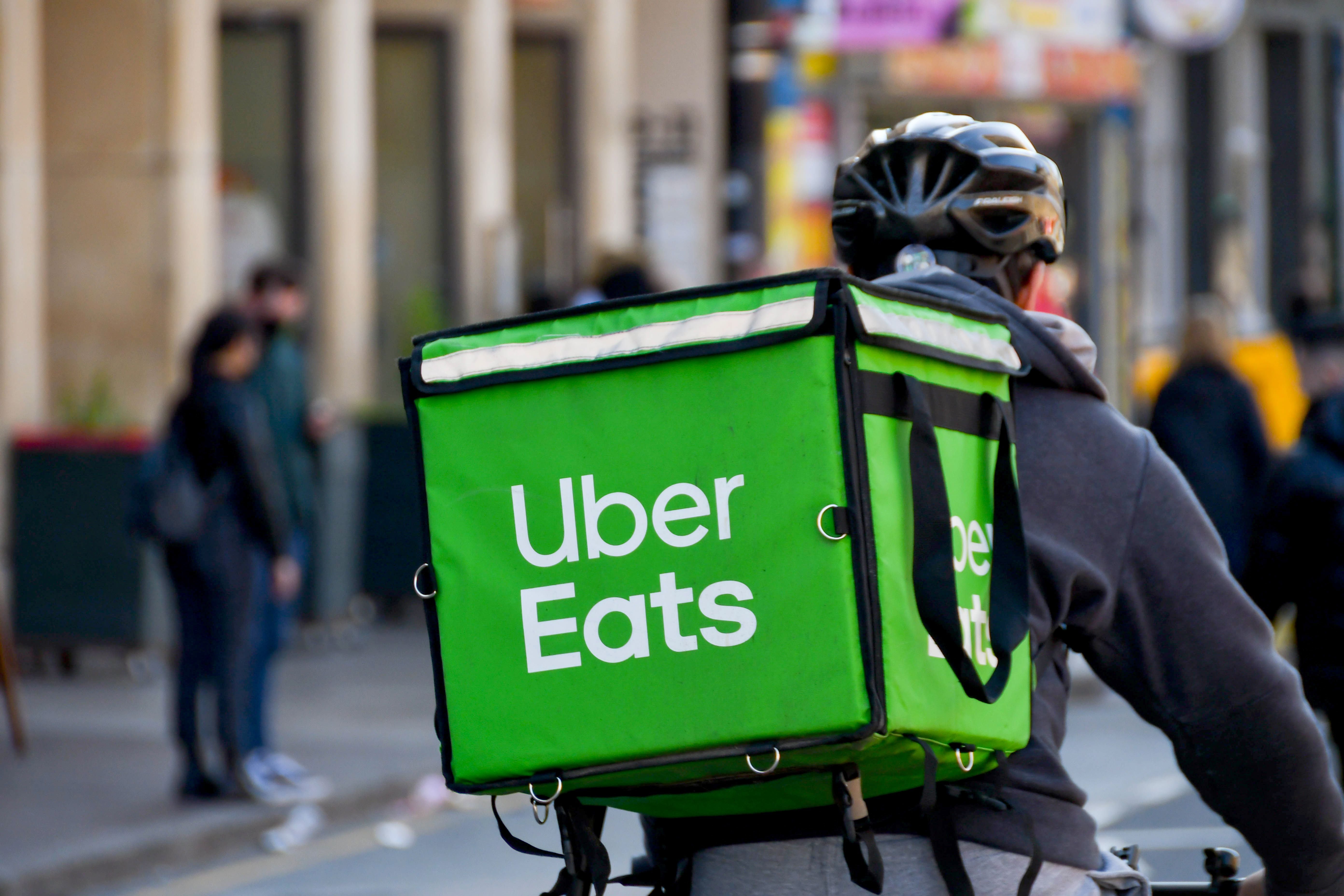 Fahrradkurier mit grünem Uber Eats-Rucksack fährt durch die Stadt.