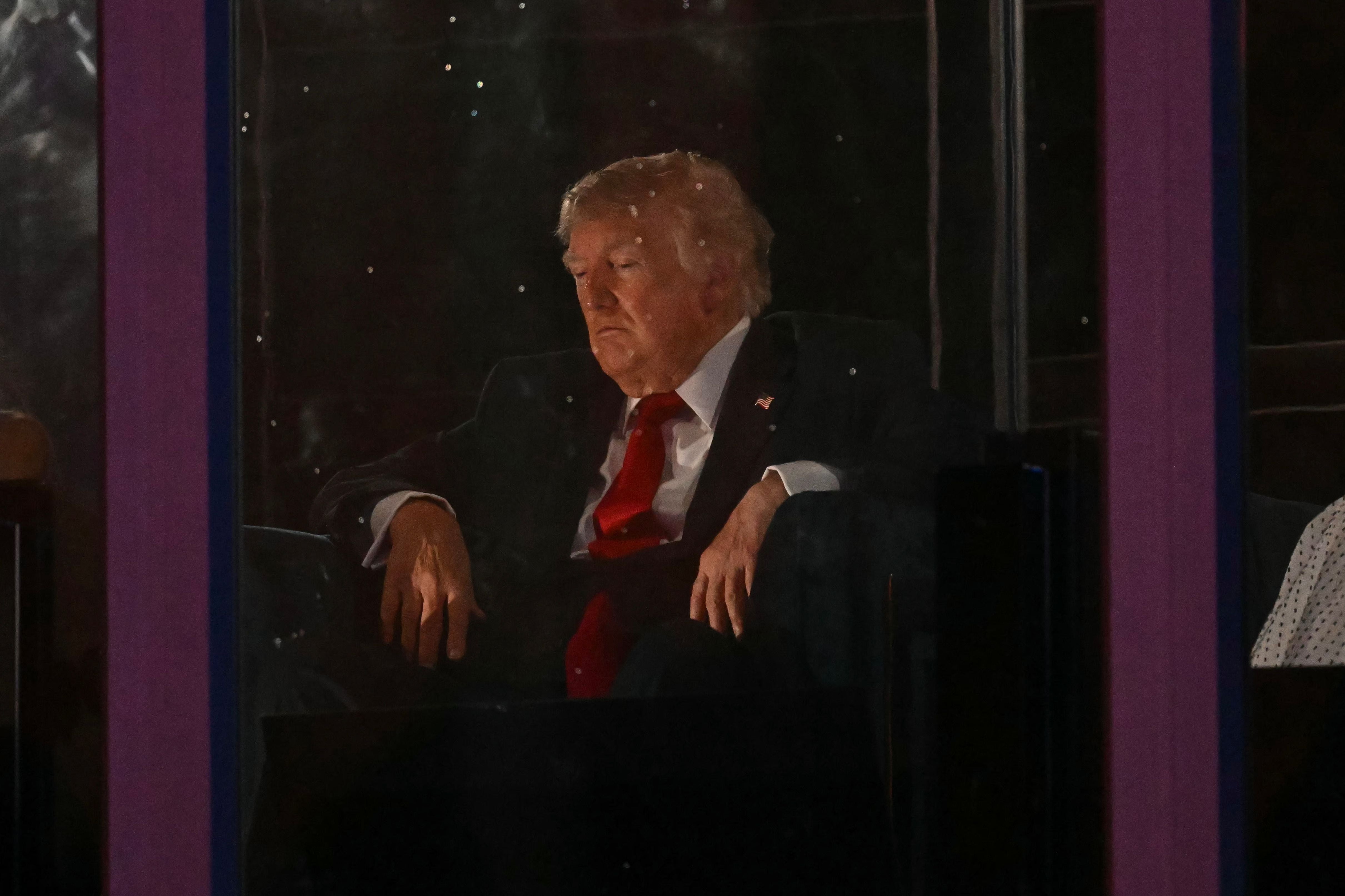 Ein älterer Mann im Anzug sitzt nachdenklich hinter Glas, im Hintergrund sind Lichter zu sehen.