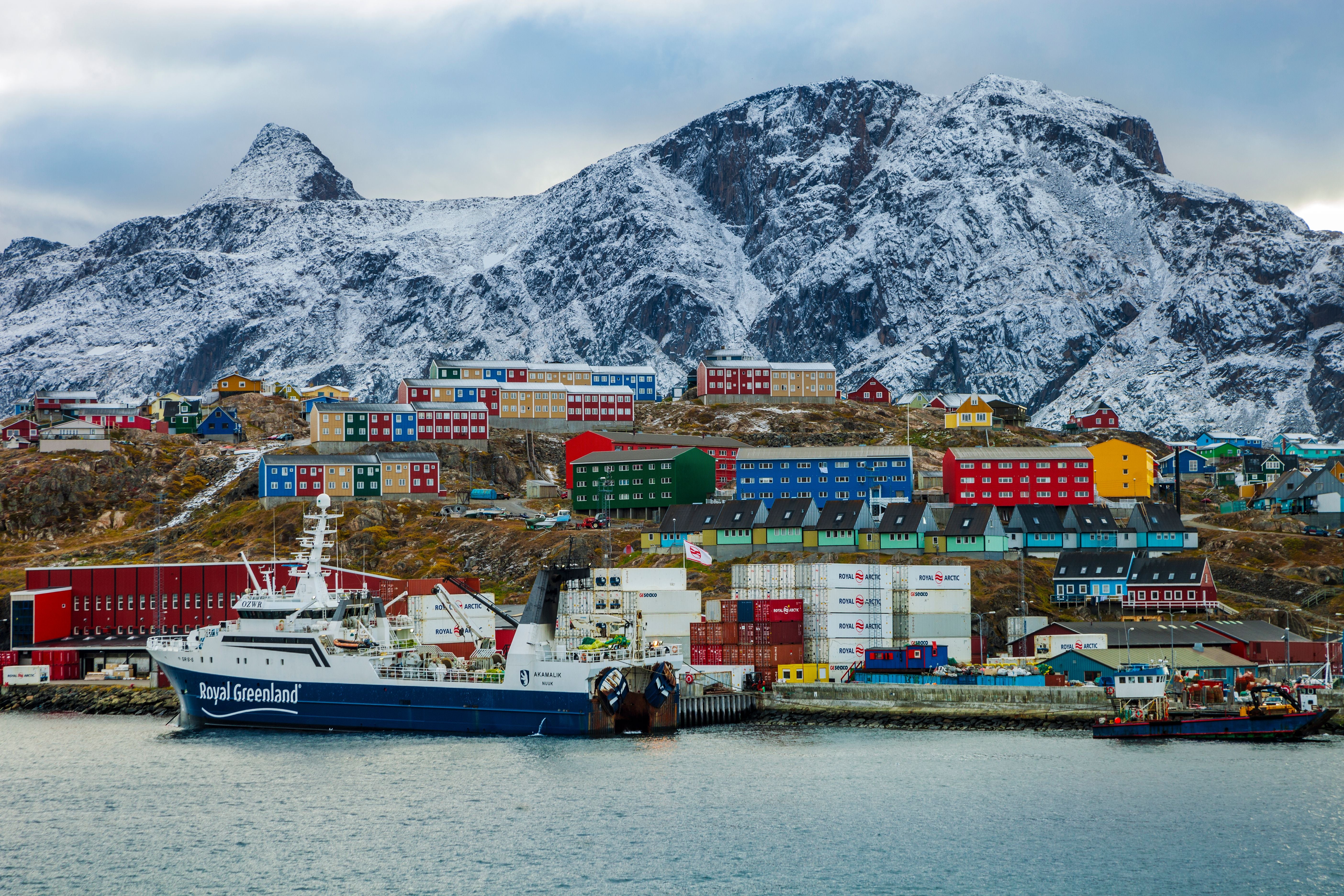 Bunte Häuser und Schiffe vor verschneiten Bergen in Sisimiut, Grönland.