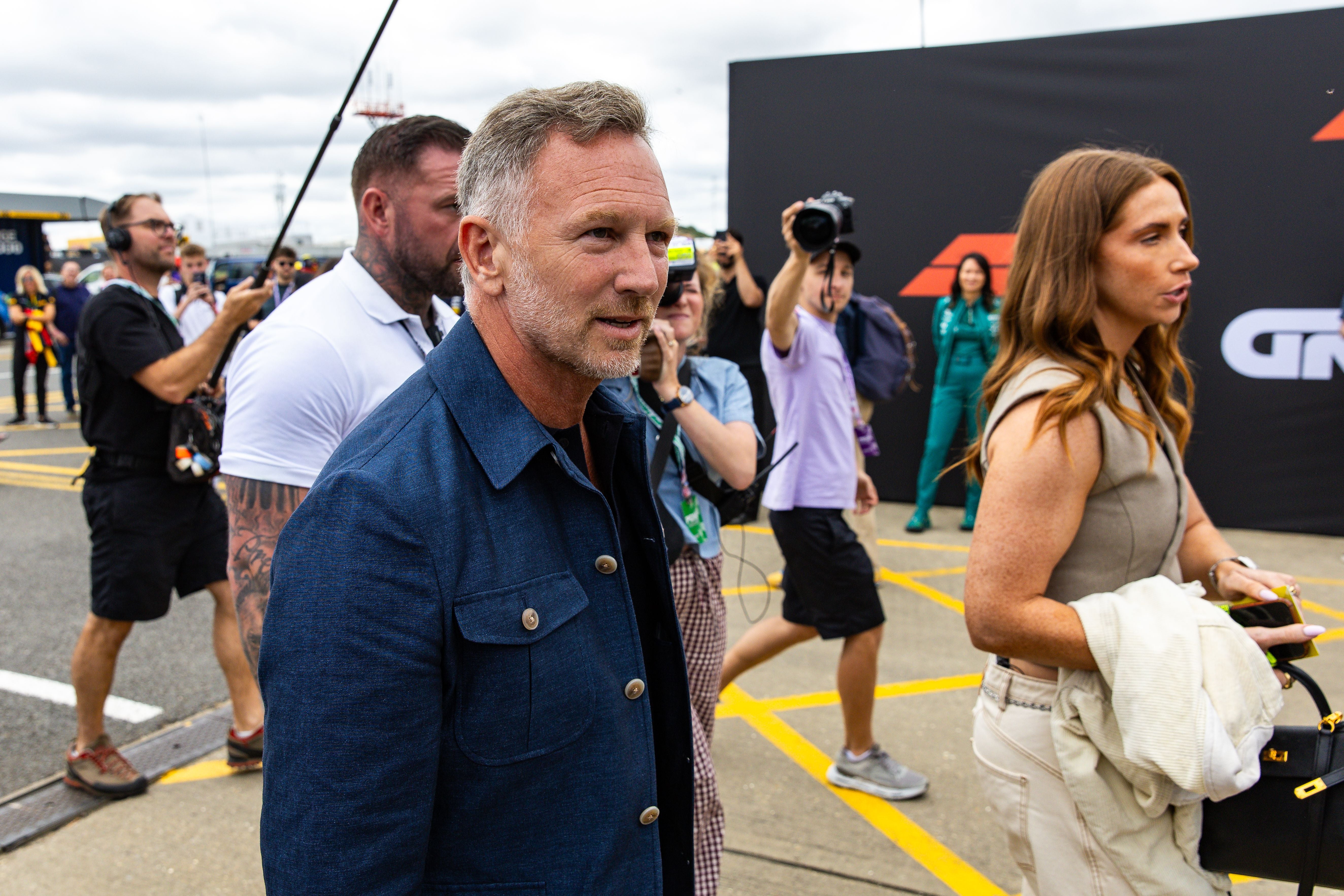 Ein Mann im blauen Jackett läuft durch das Fahrerlager bei einem Formel-1-Event, Menschen um ihn herum.