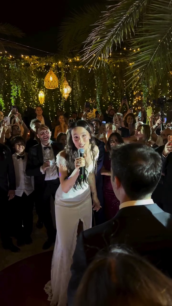 Braut singt ihrem Bräutigam auf einer beleuchteten Hochzeitsparty vor Gästen ein Lied.