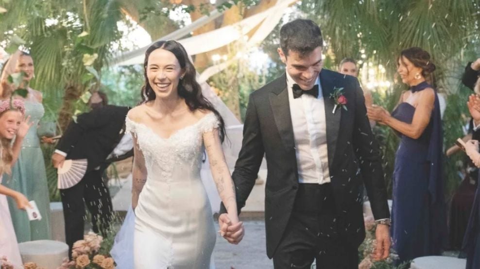 Braut und Bräutigam lächelnd bei ihrer Hochzeit, umgeben von gratulierenden Gästen.