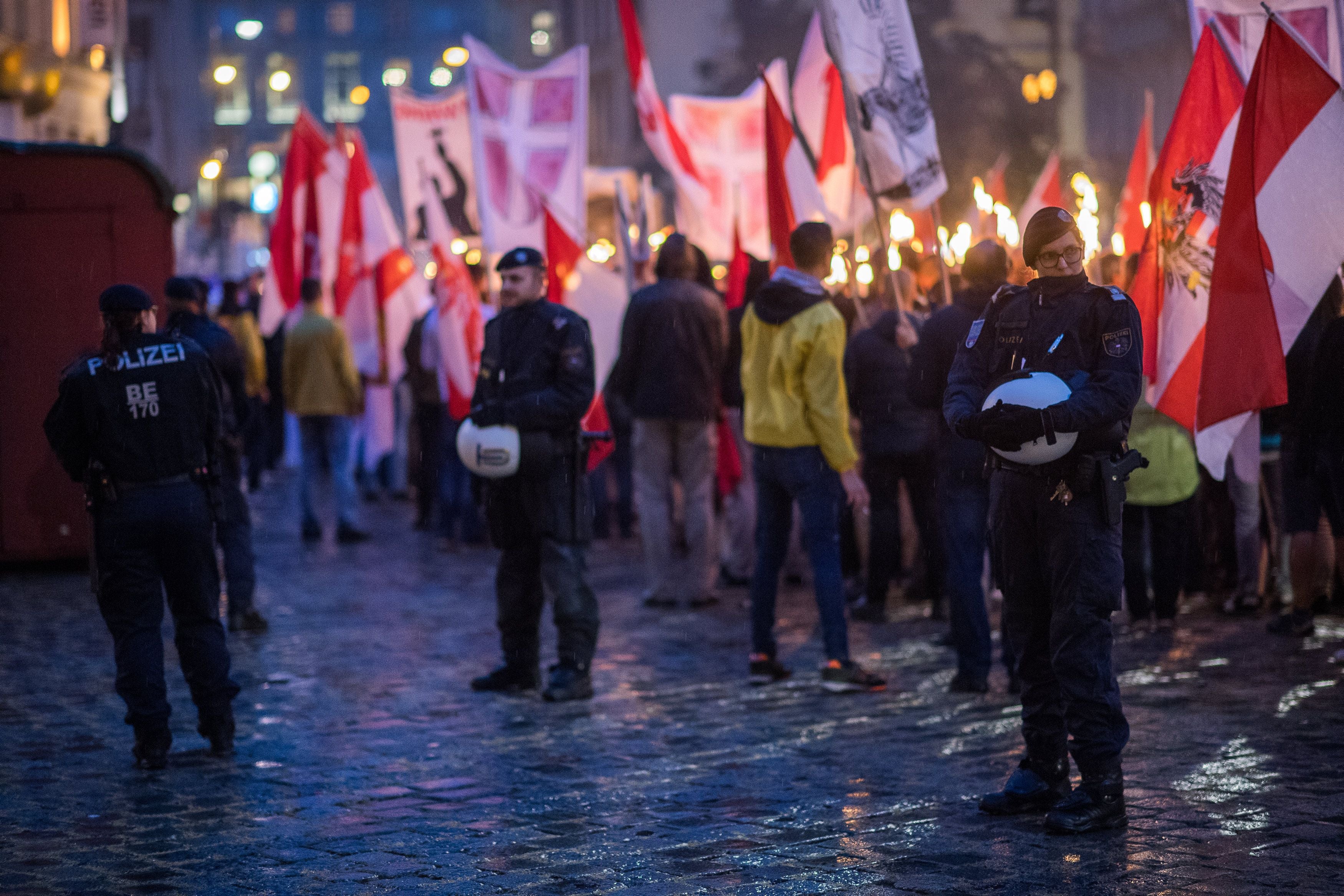 Polizisten sichern eine Kundgebung mit vielen Menschen, österreichischen Fahnen und Fackeln bei Nacht.