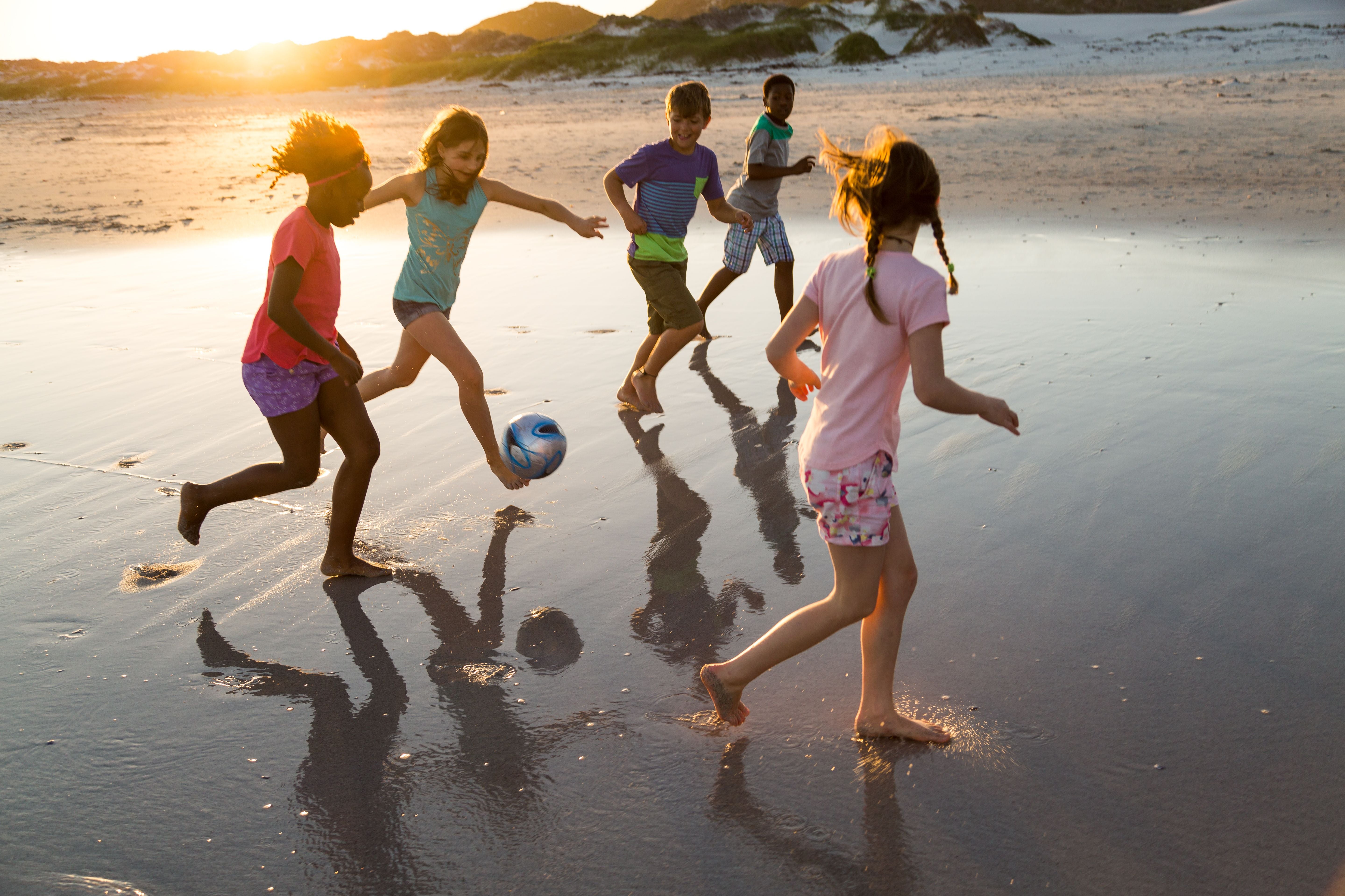 Group of children playing soccer together on a beach at sunset
