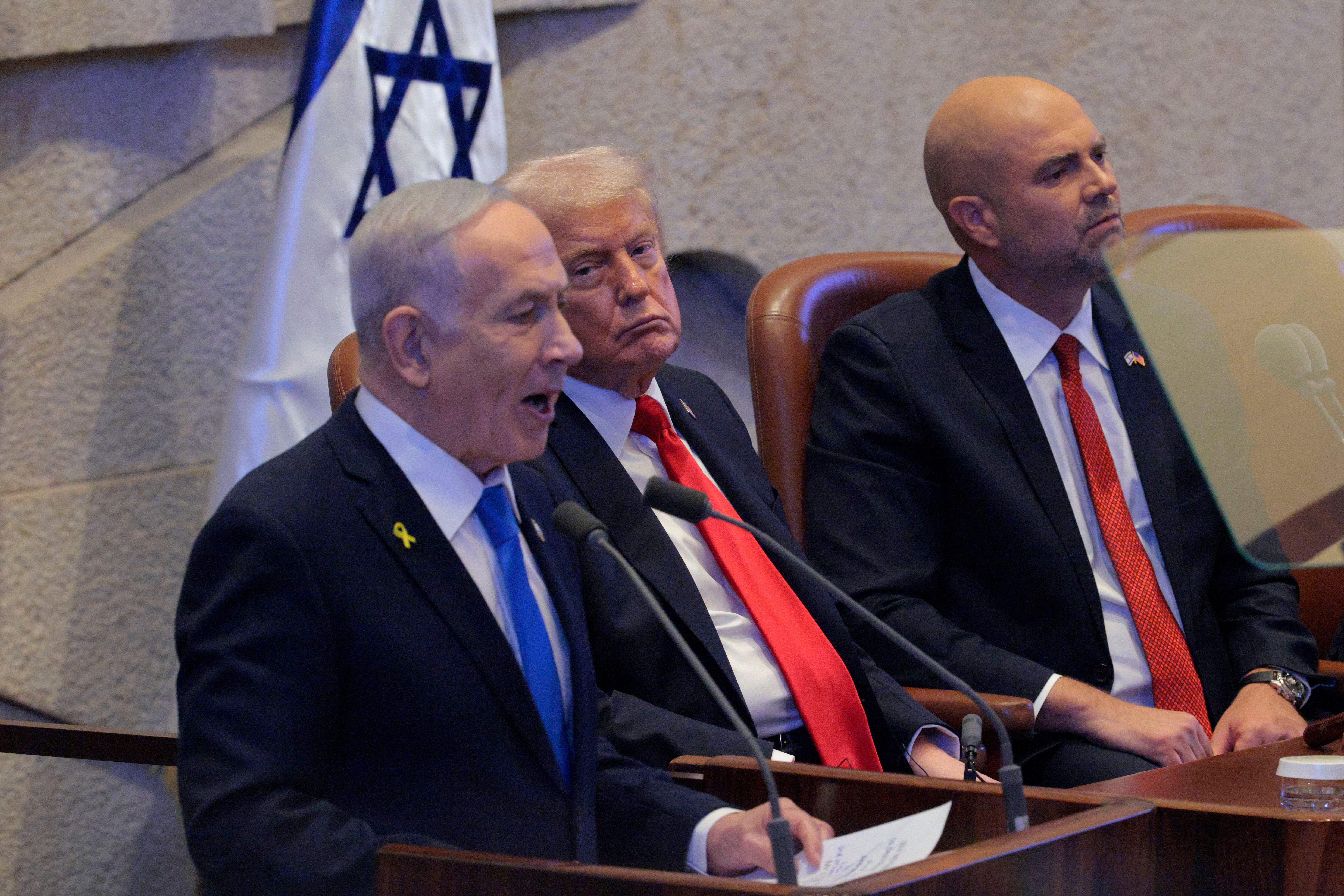 Benjamin Netanjahu spricht in der Knesset, Donald Trump und ein weiterer Mann hören zu.