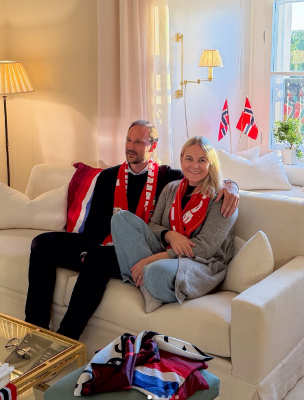 Ein Paar sitzt auf einem Sofa, trägt Fanschals und wird von norwegischen Flaggen umgeben.
