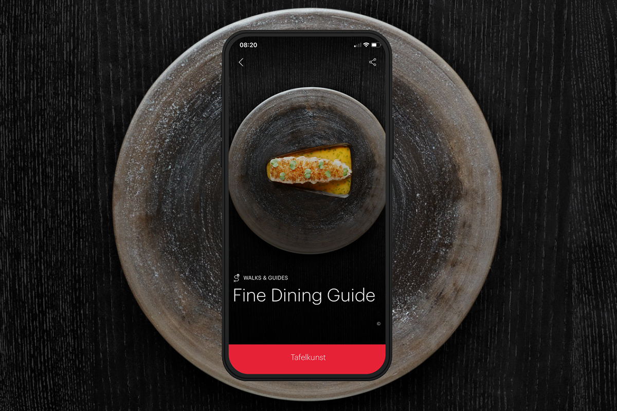 Smartphone zeigt einen Fine Dining Guide vor einem kunstvoll angerichteten Gericht auf einem Teller.