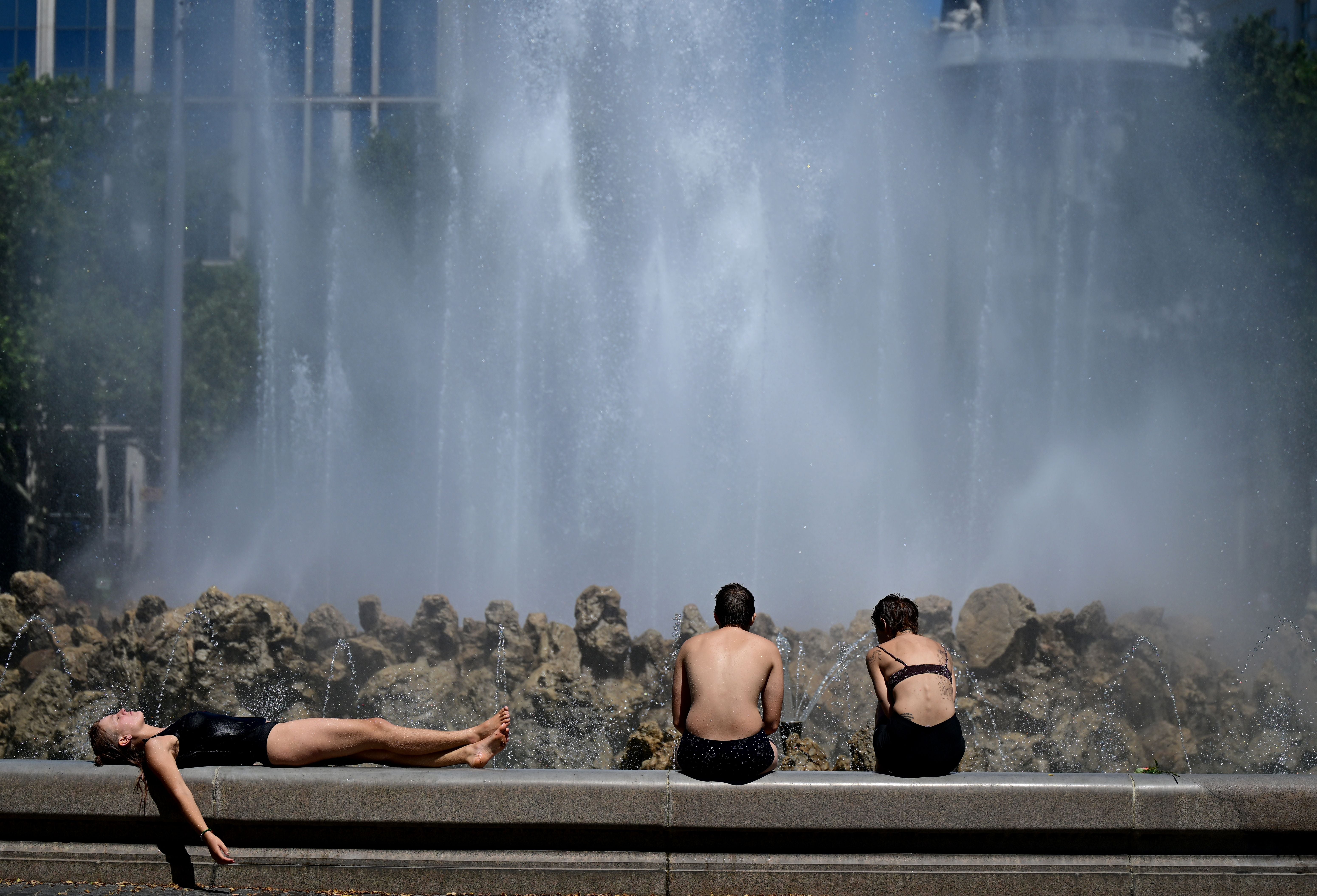 Drei junge Menschen kühlen sich bei Hitze am Hochstrahlbrunnen in Wien ab.