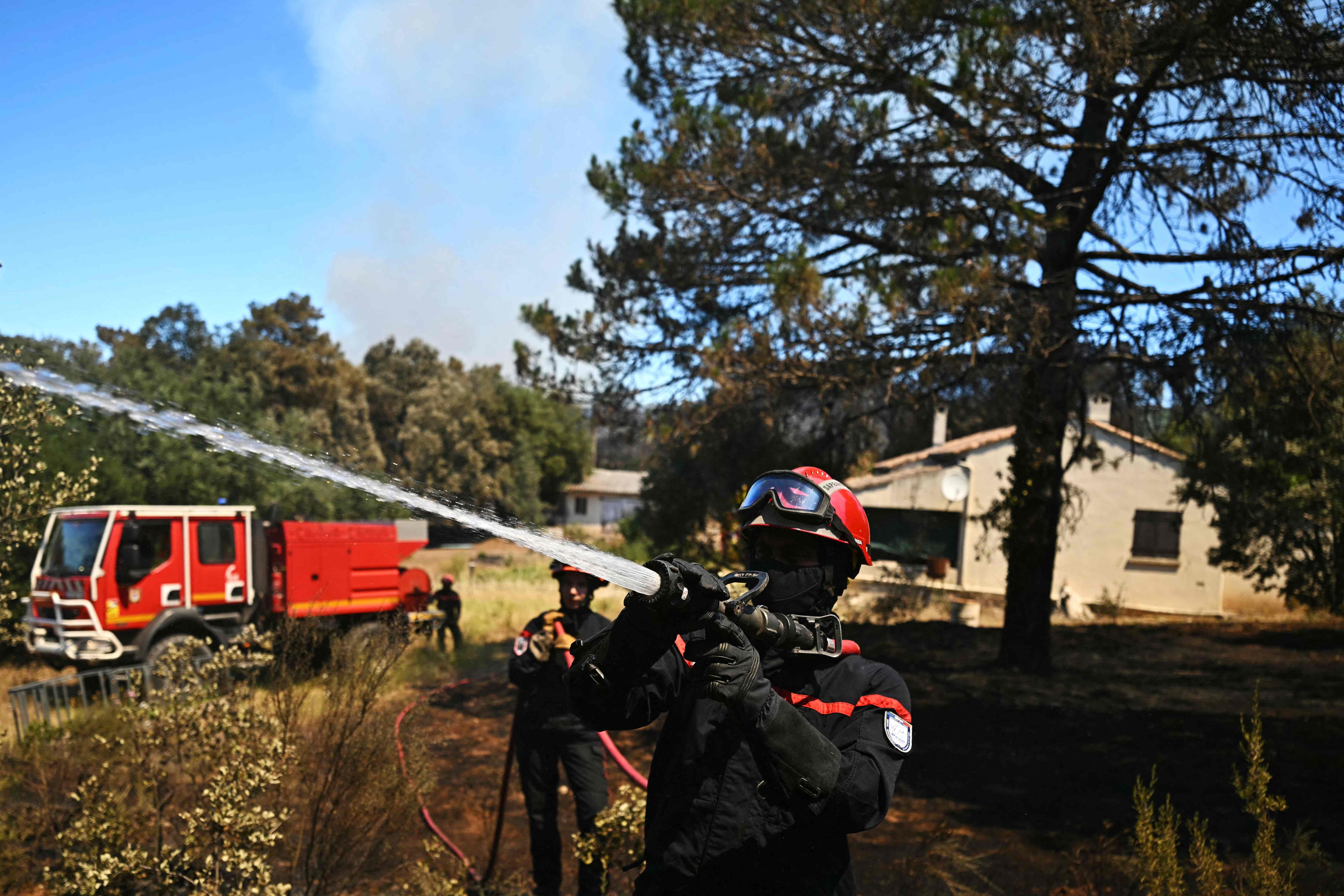 A firefighter extinguishes a wildfire next to a house in the southern France department of Herault as 700 hundred firefighters backed by special aircraft battled to control a 'gigantic' blaze in nearby department of Pyrenees-Orientales, near the town of Carlencas-et-Levas on July 6, 2026. Wildfires raged across southern Europe, forcing thousands of people to evacuate their homes and prompting officials to ban spectators from a stage of the storied Tour de France cycling race. (Photo by Gabriel BOUYS / AFP)