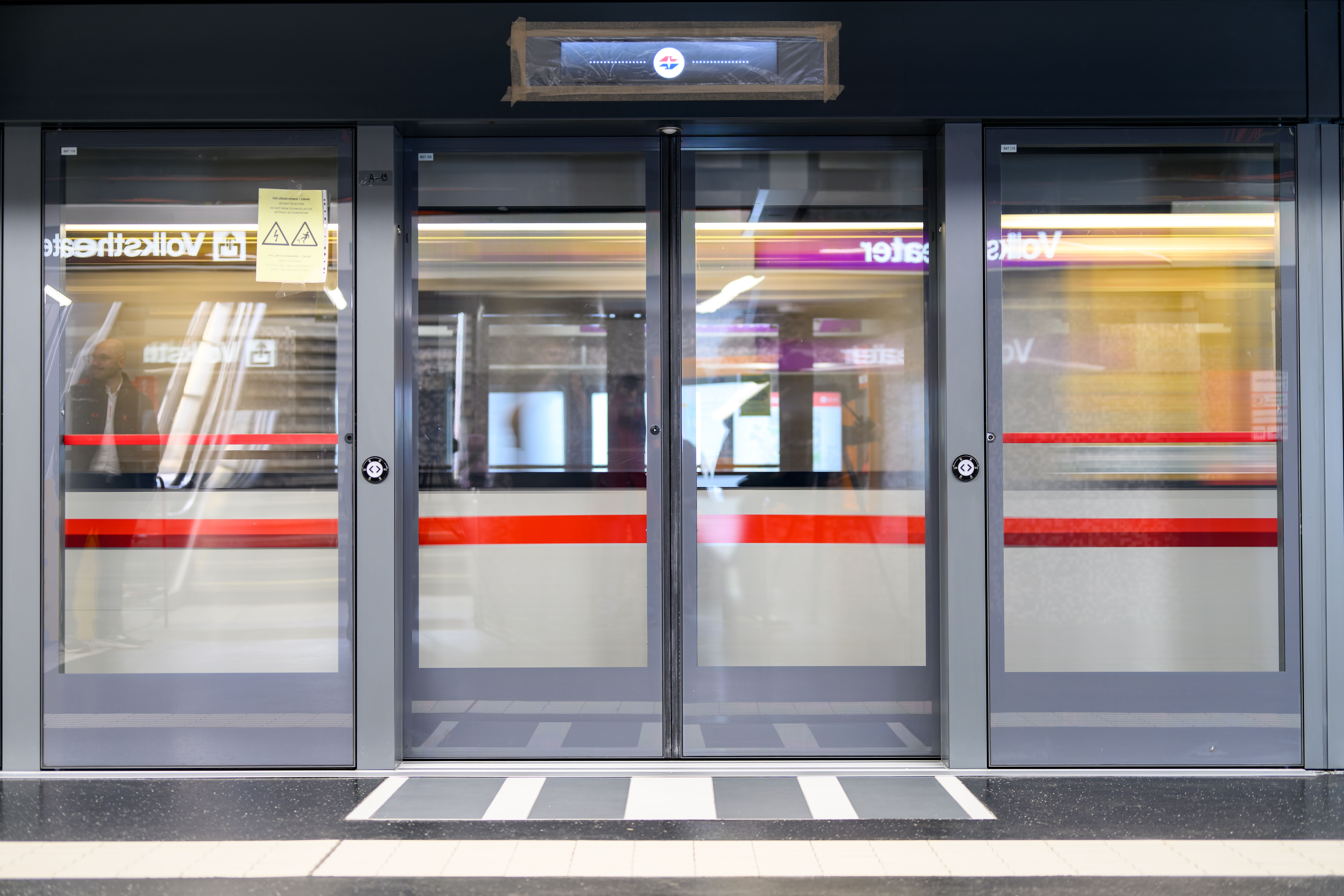 Glasverschlossene Bahnsteigtüren in der U-Bahn-Station Volkstheater in Wien, Zug fährt vorbei.