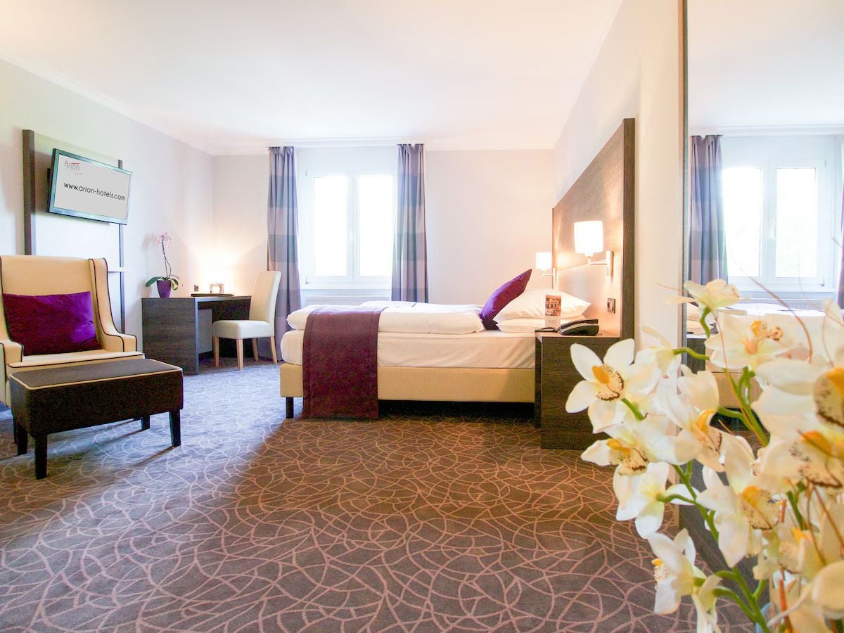 Modernes Hotelzimmer mit Doppelbett, Sessel, Schreibtisch und großen Fenstern im Arion City Hotel.