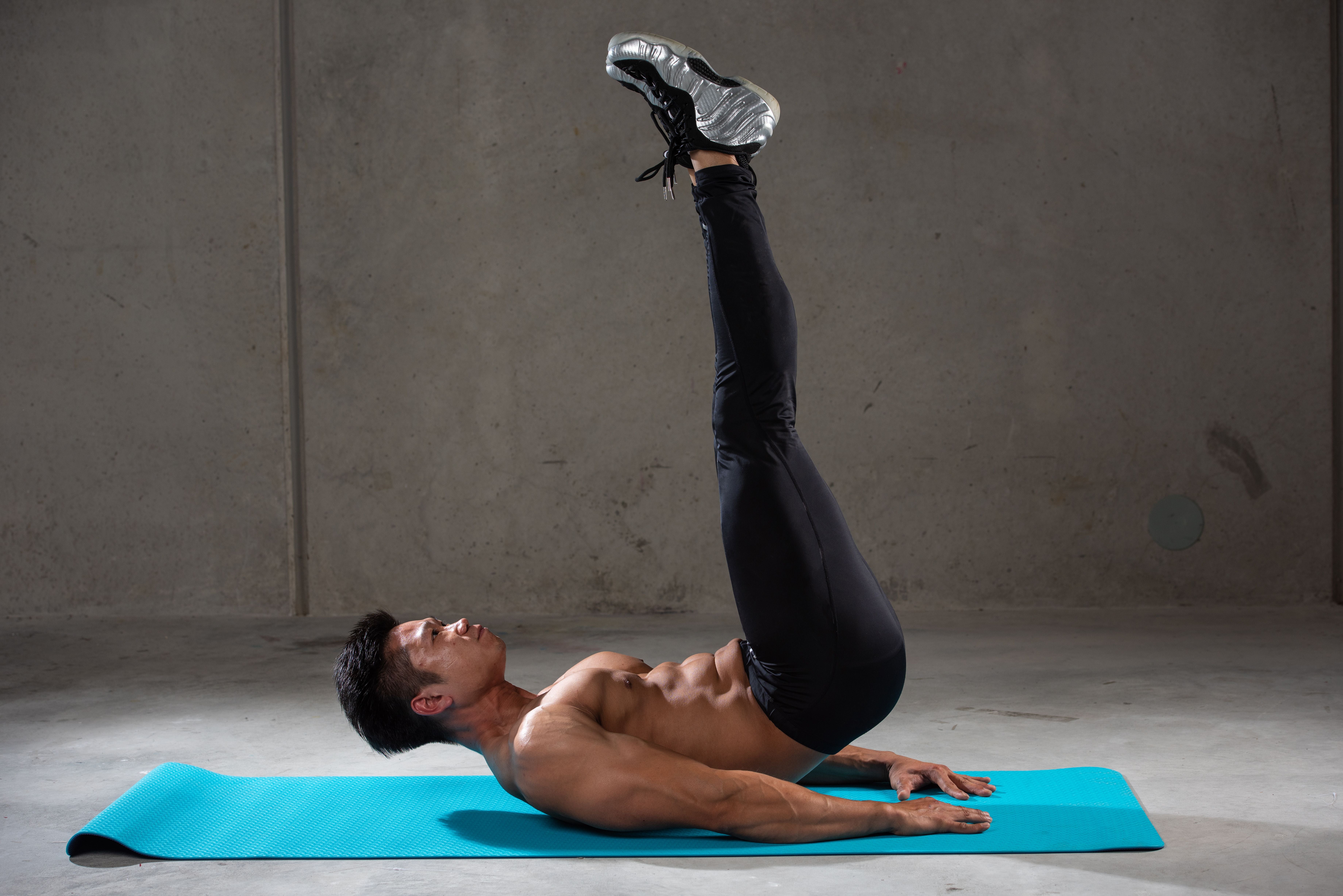 Mann macht Beinheben als Bauchmuskel-Übung auf einer blauen Matte im Fitnessstudio.