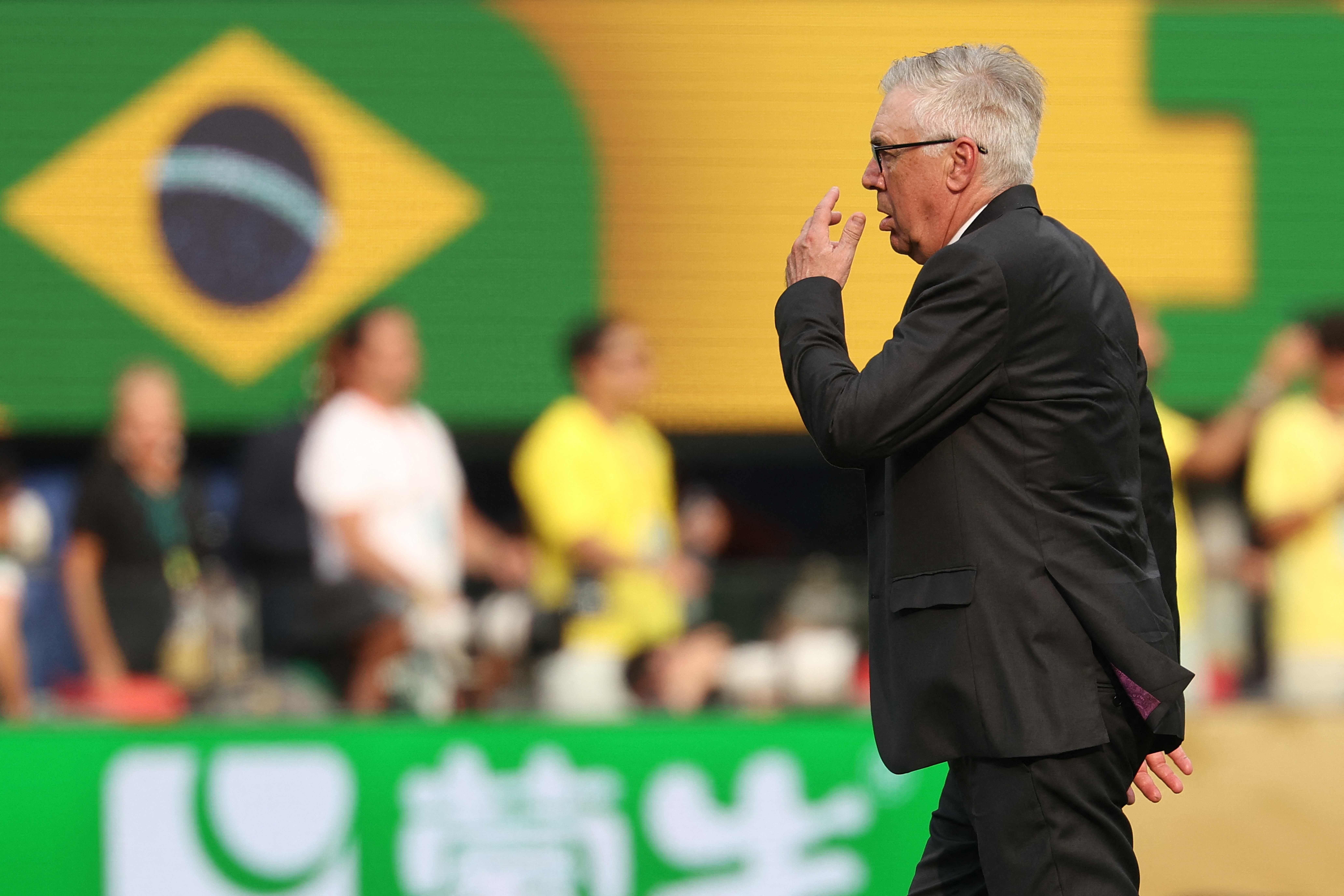 Ein Mann im Anzug reagiert enttäuscht vor einer brasilianischen Flagge im Stadion.
