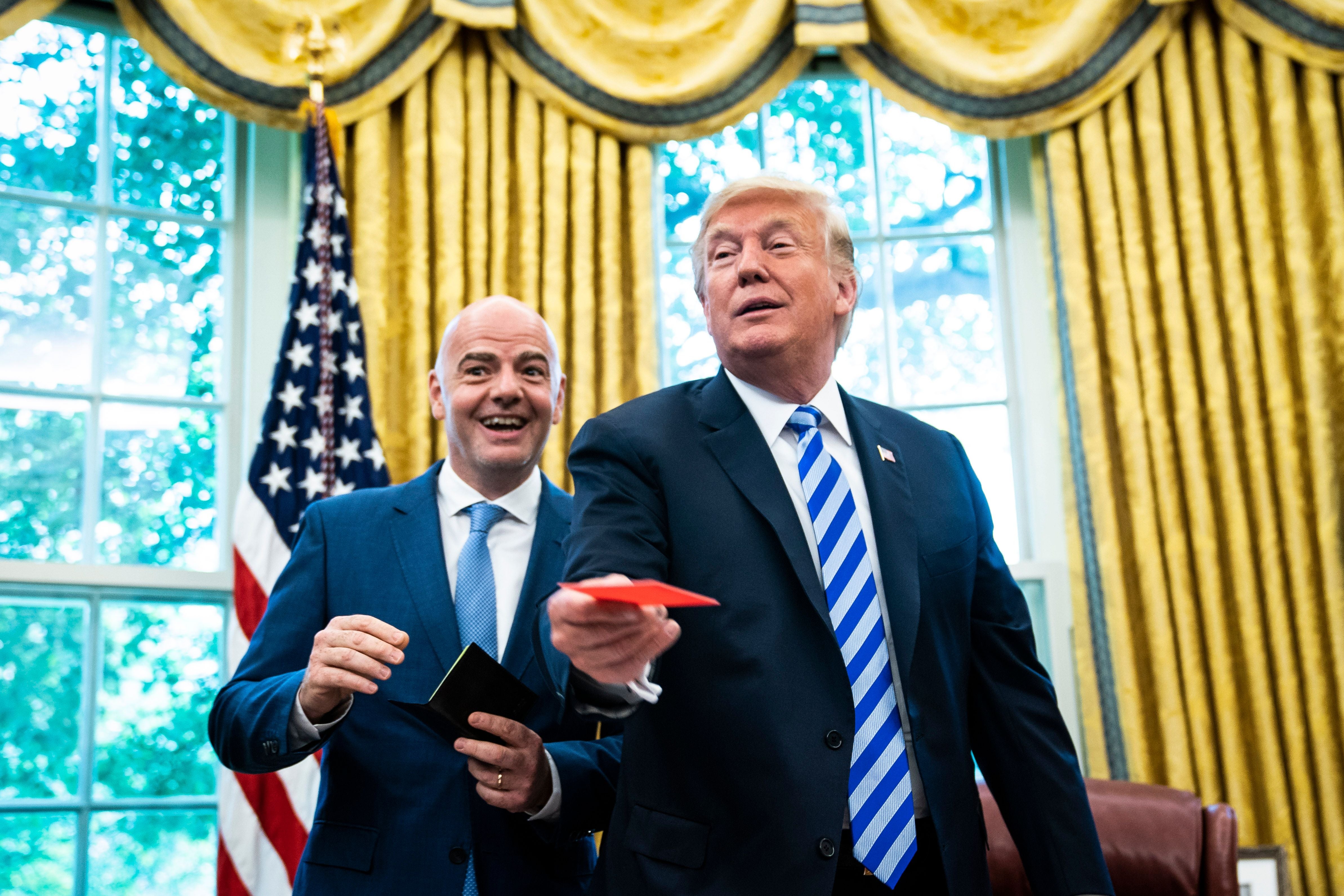 Donald Trump erhält im Oval Office von Gianni Infantino eine rote Karte, beide lachen.