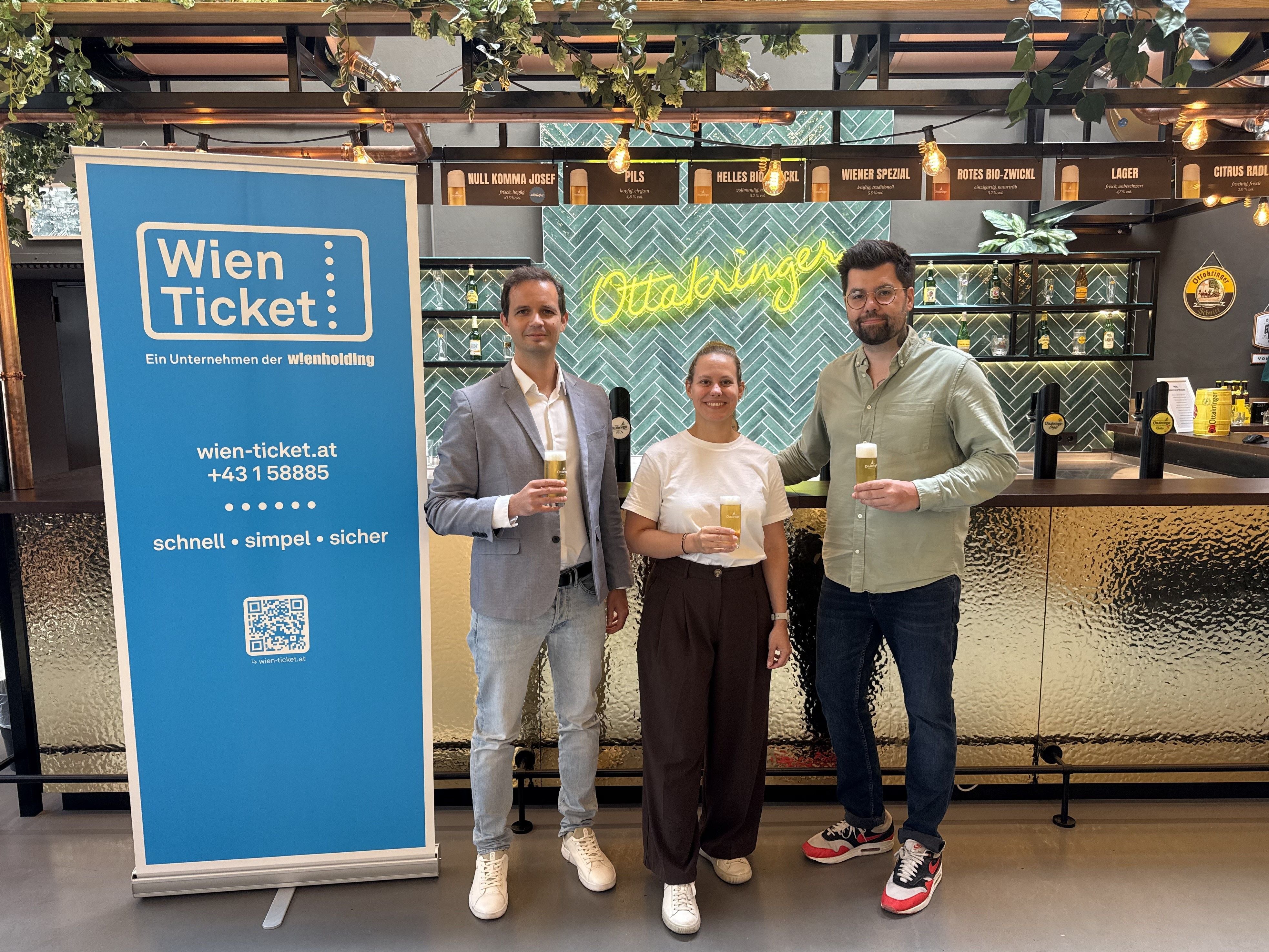 Drei Personen stehen vor einer Bar und halten Biergläser, links ein Wien Ticket Banner.