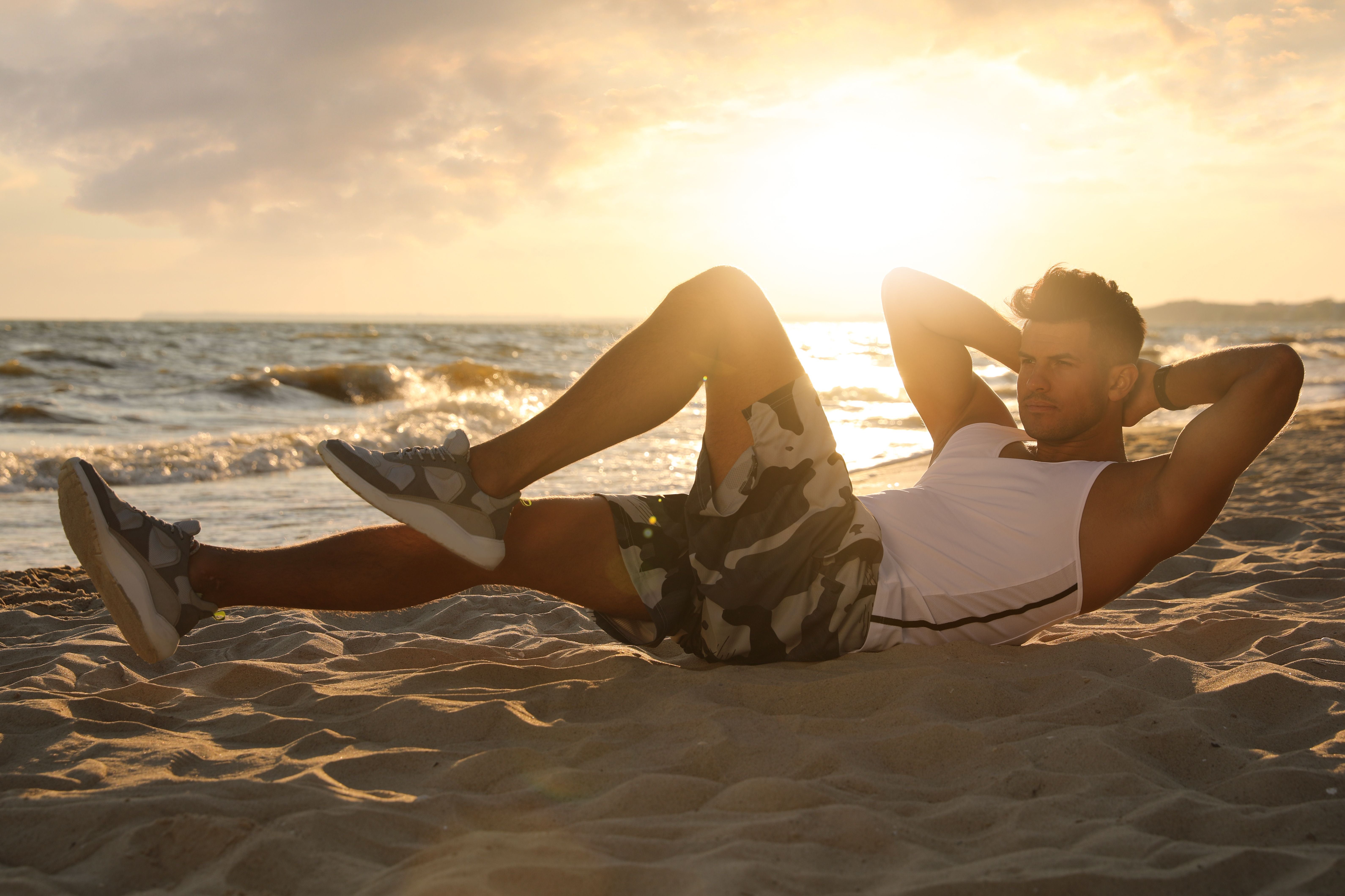 Sportlicher Mann macht am Strand Sit-ups bei Sonnenuntergang.