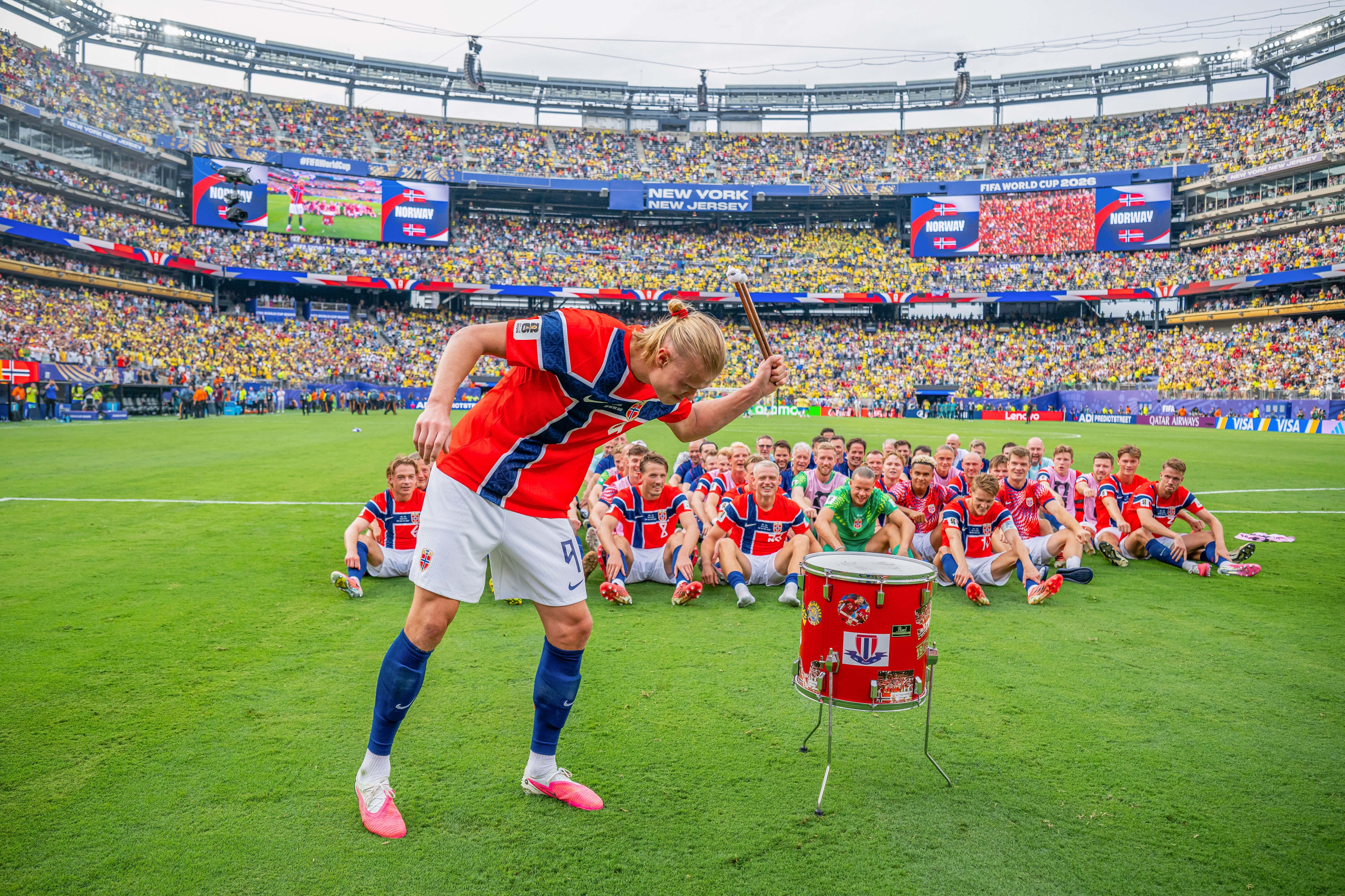 Ein norwegischer Fußballspieler schlägt auf eine Trommel, das Team jubelt im Hintergrund.