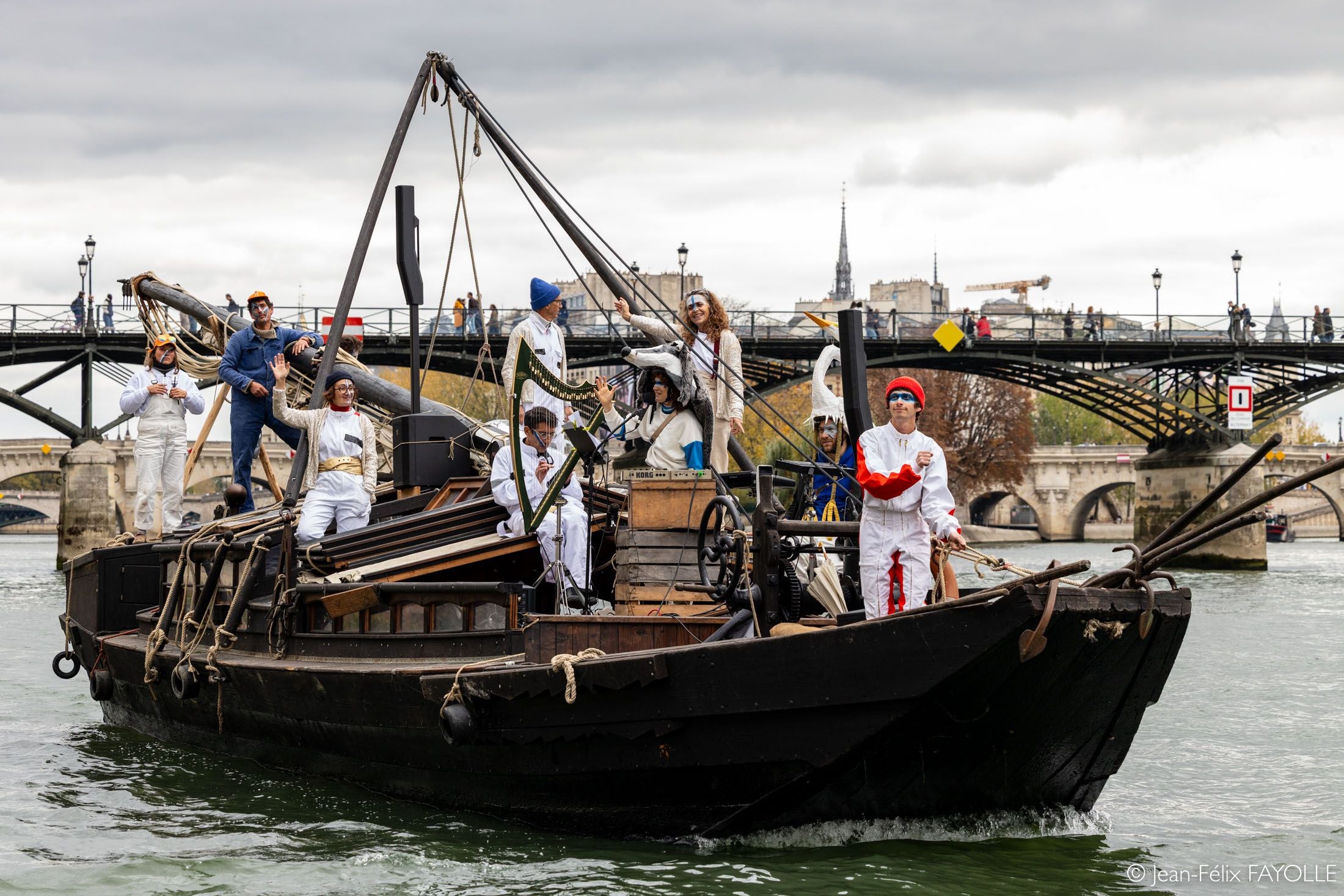 Menschen in Kostümen stehen auf einem traditionellen Boot auf einem Fluss in einer Stadt.